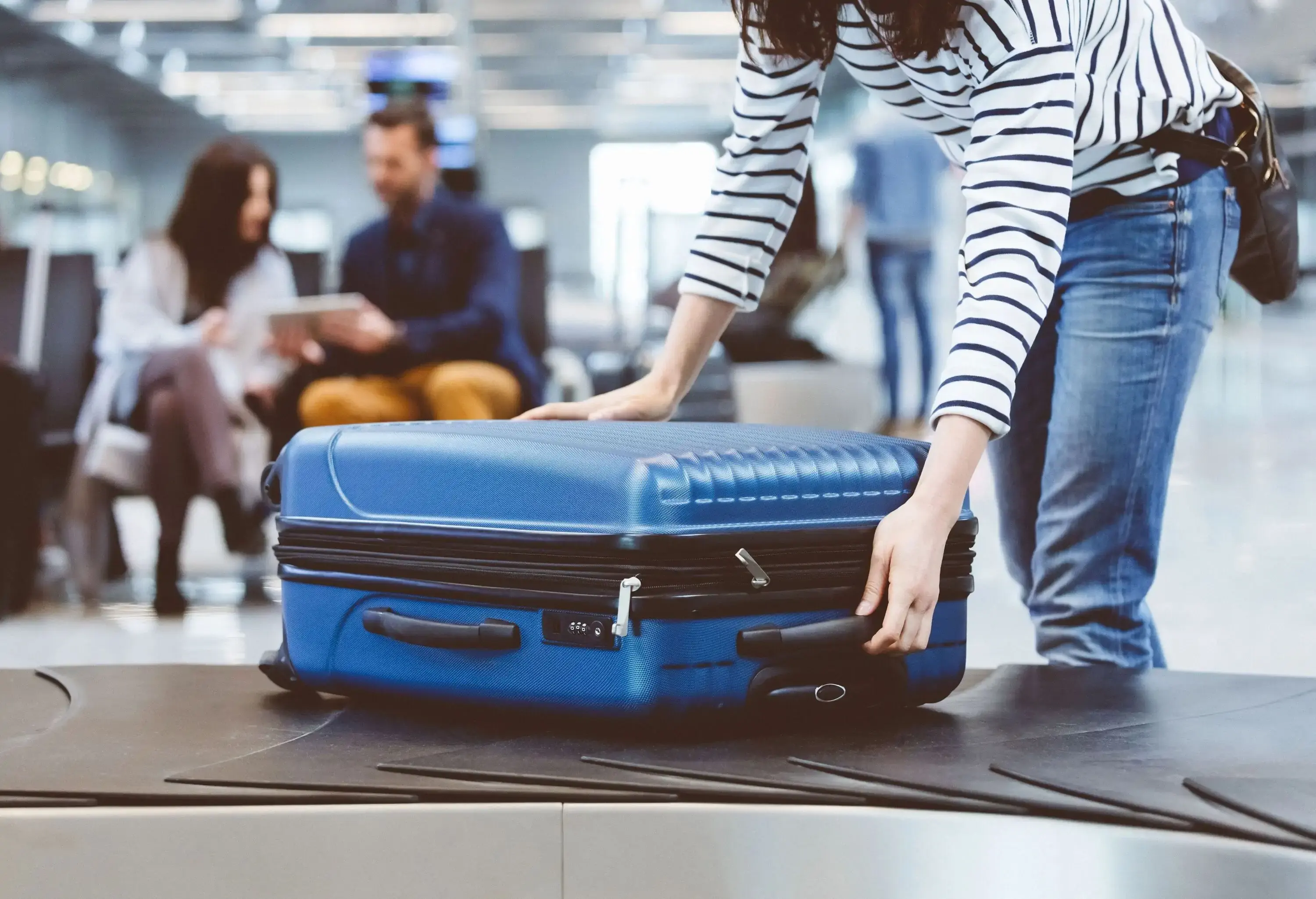A women picking up her carry-on suitcase from the airport