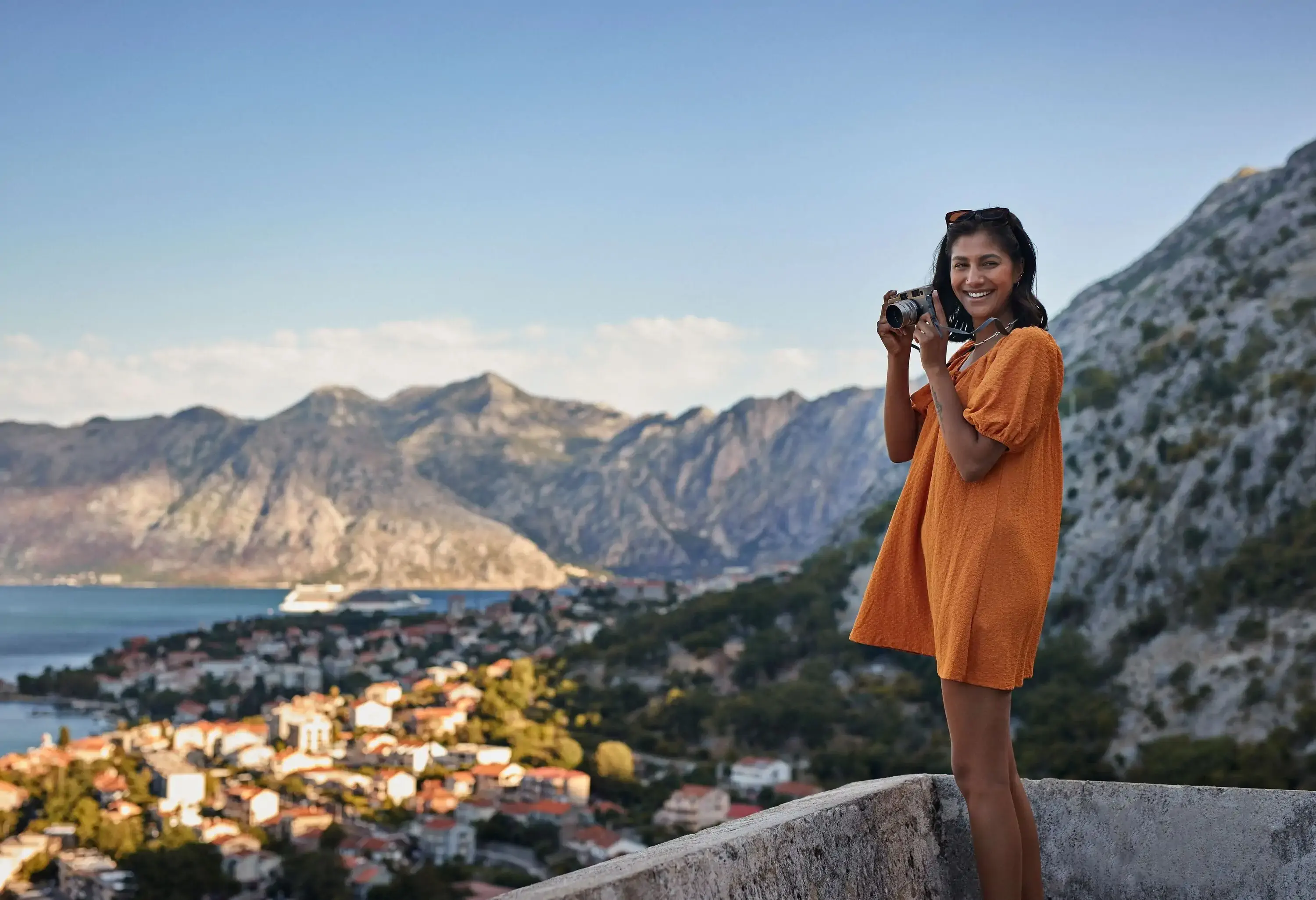Happy young woman with camera standing against mountain range near town