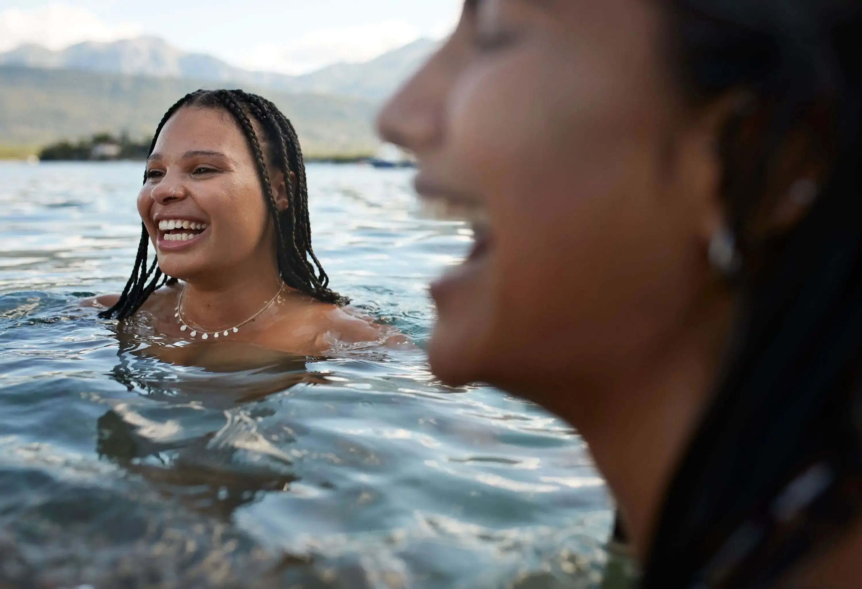Happy young woman with braided hair by female friend in bay