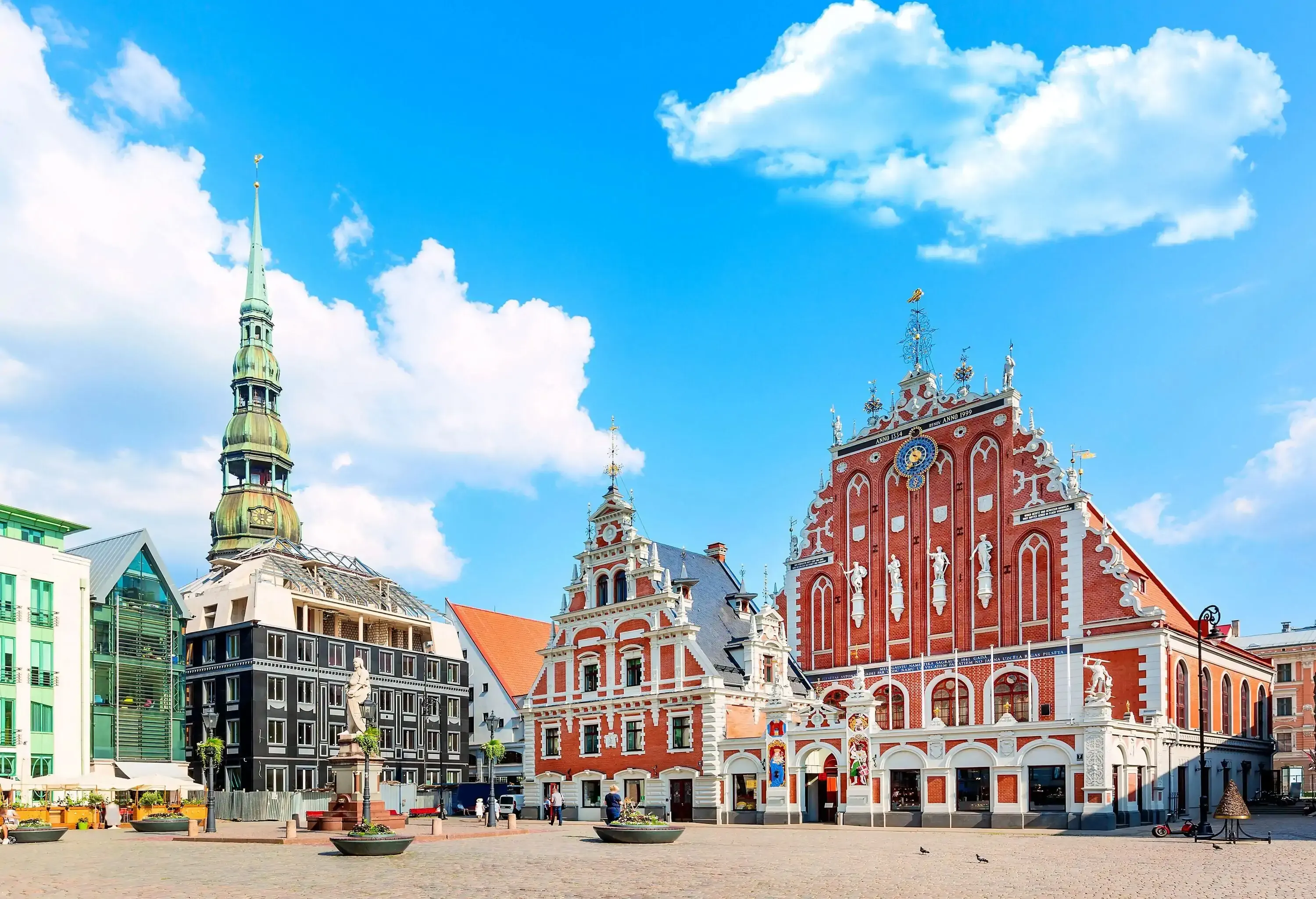 A cobbled square with a white statue surrounded by colourful buildings dominated by a tower.