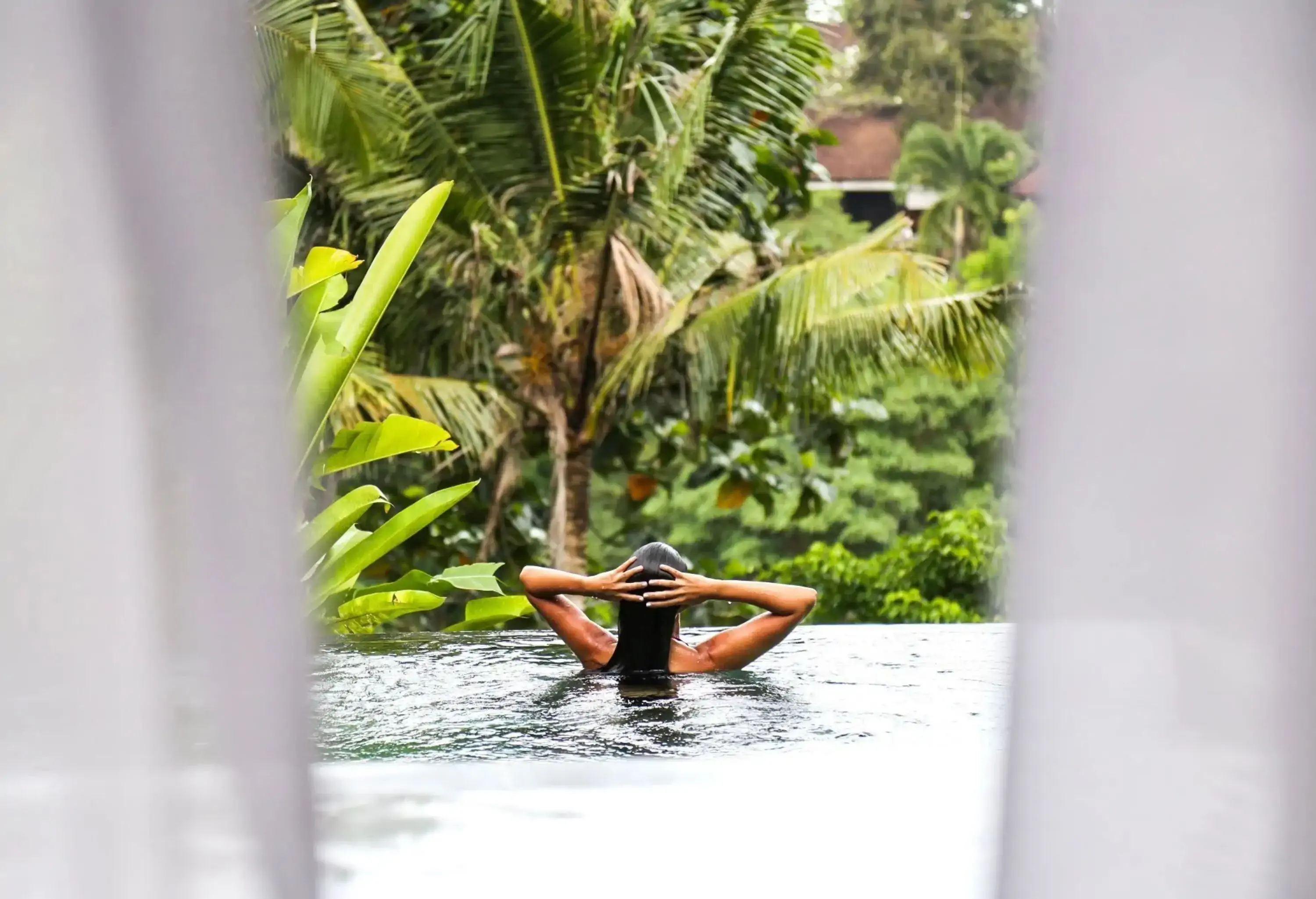 A woman swimming in an infinity pool surrounded by tropical trees.