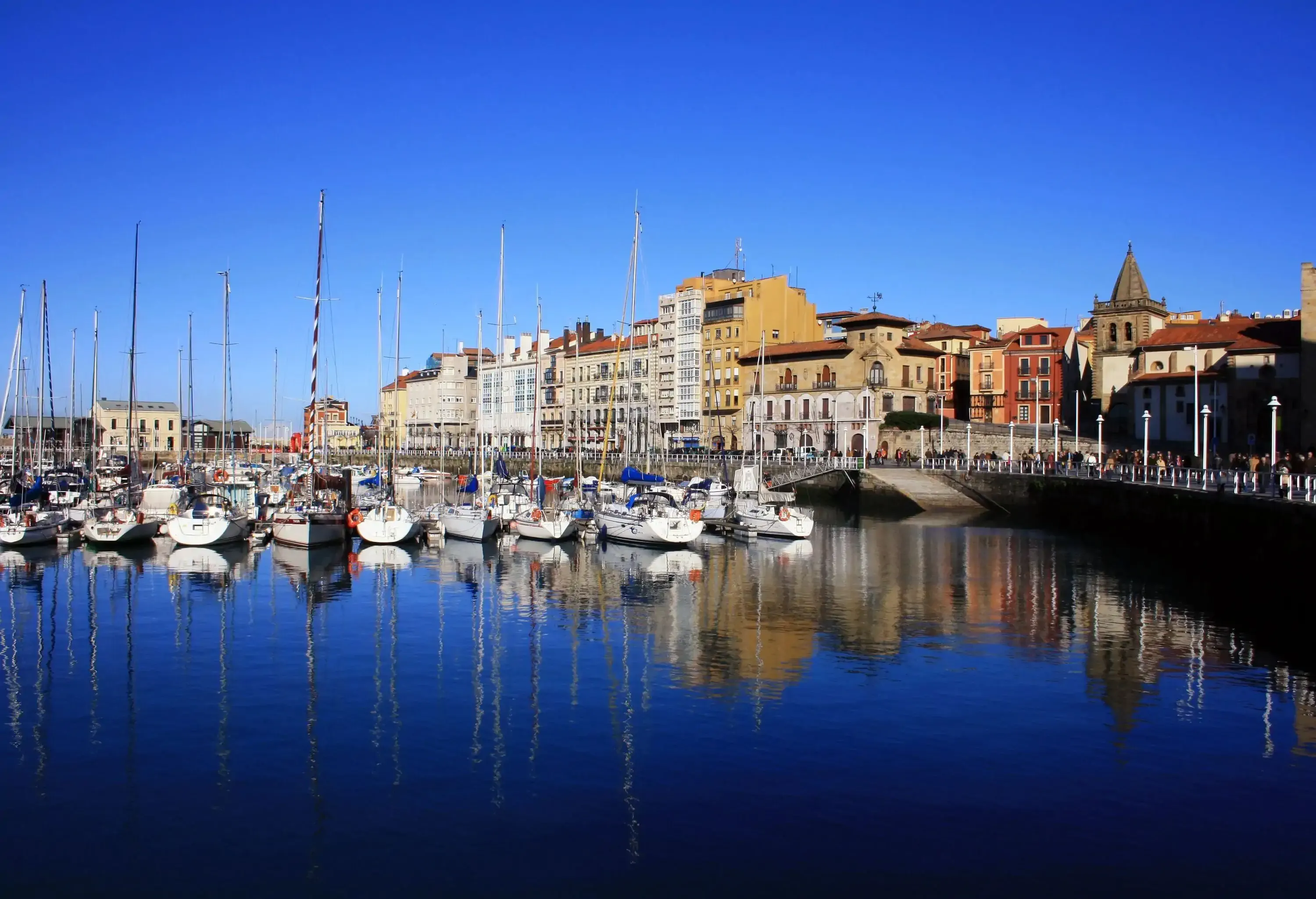 Fishing boats moored in the marina flanked with classic buildings against the blue sky.