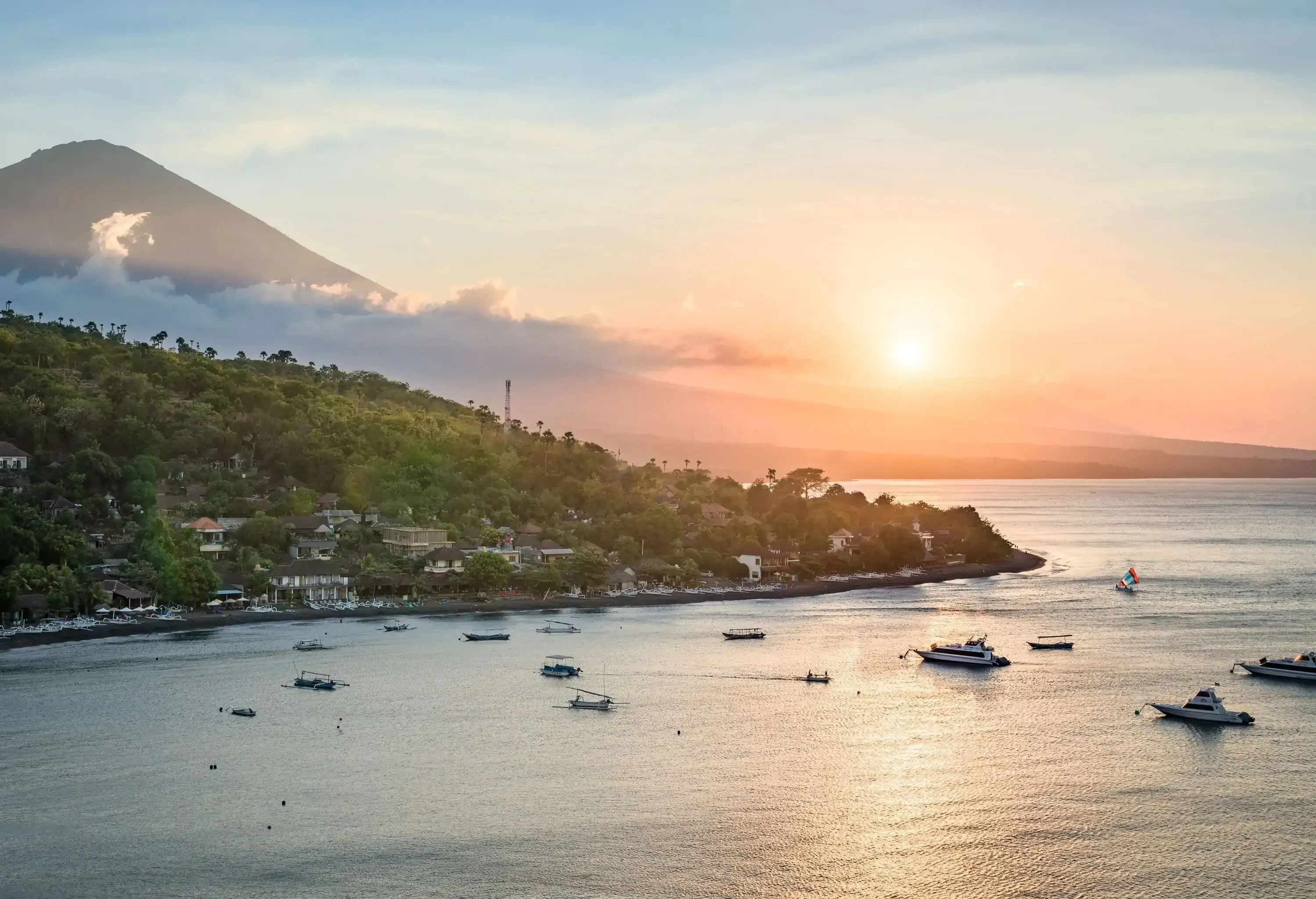 Boats sailing across the sea as the sun rises over the mountains in the distance.
