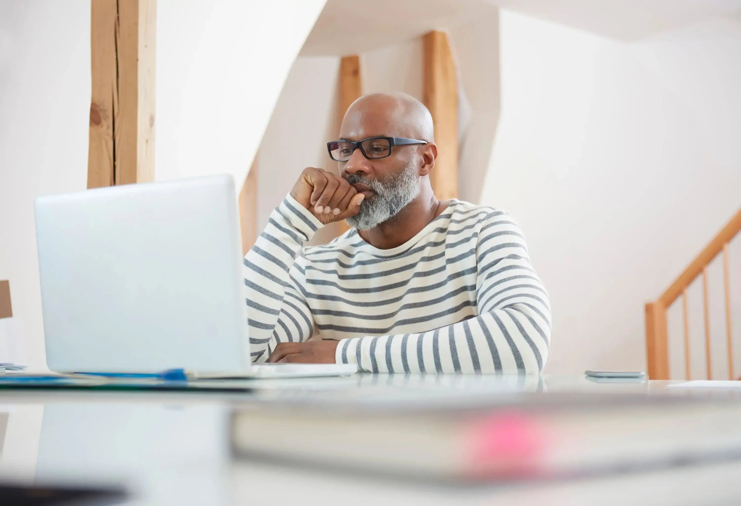 A man in glasses and striped sweater watches something on a white laptop.