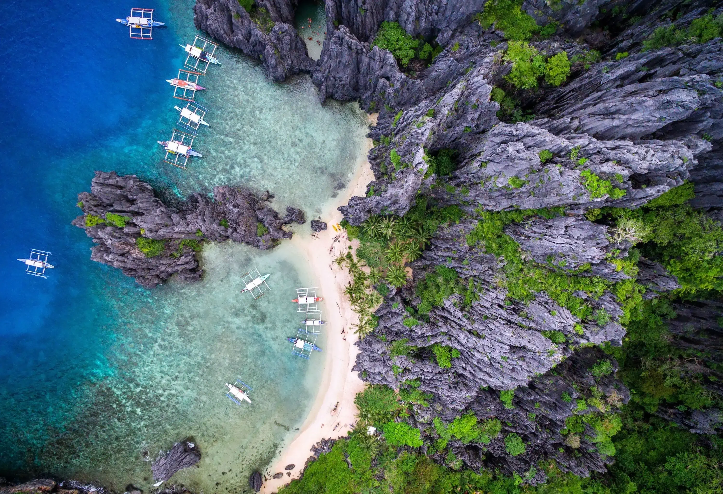 Passenger boats docked along the powdery white sand beach with crystal clear turquoise enclosed by tall, towering limestone rock formations.