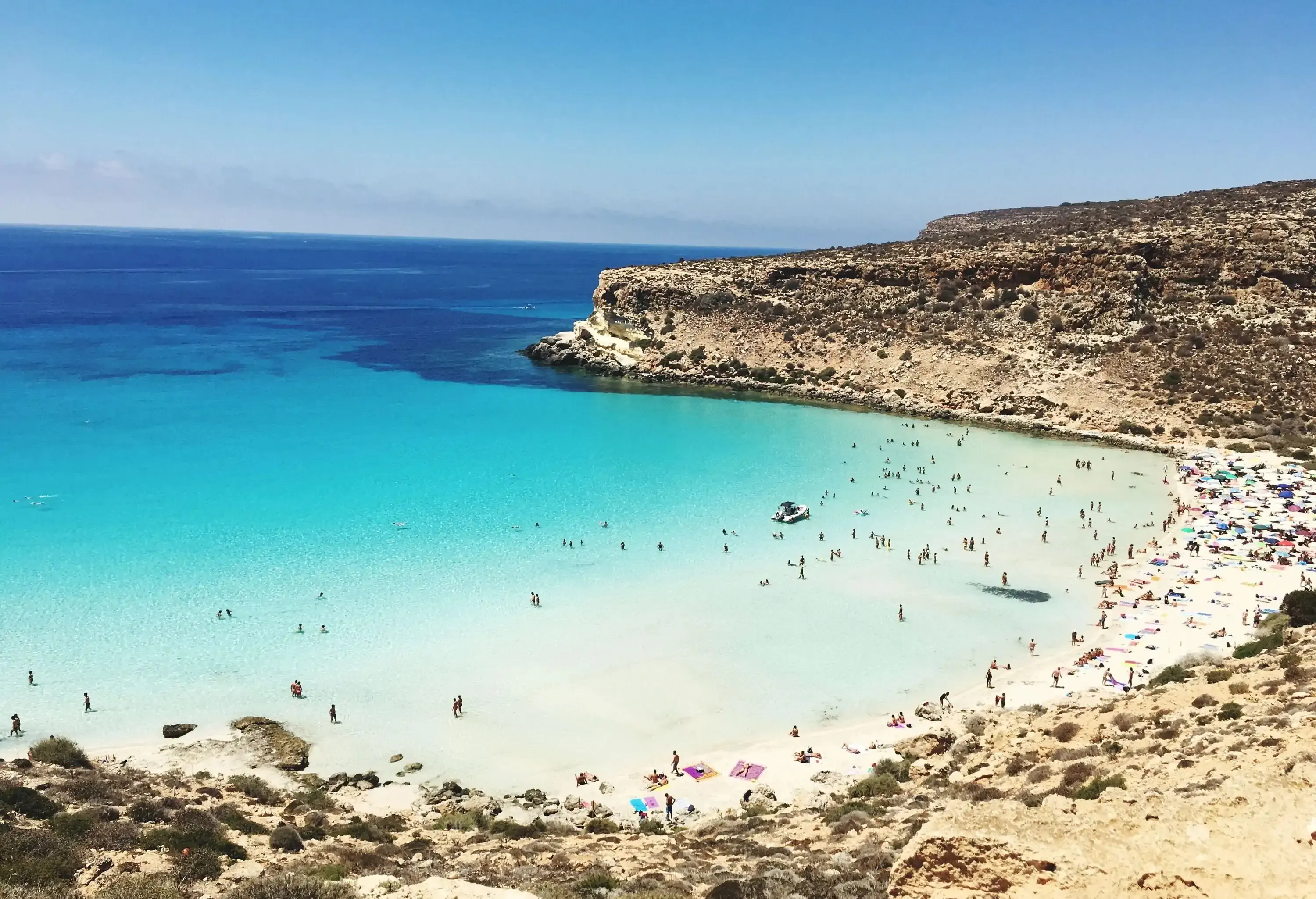 A crowded beach along a sloping and rugged coastline.