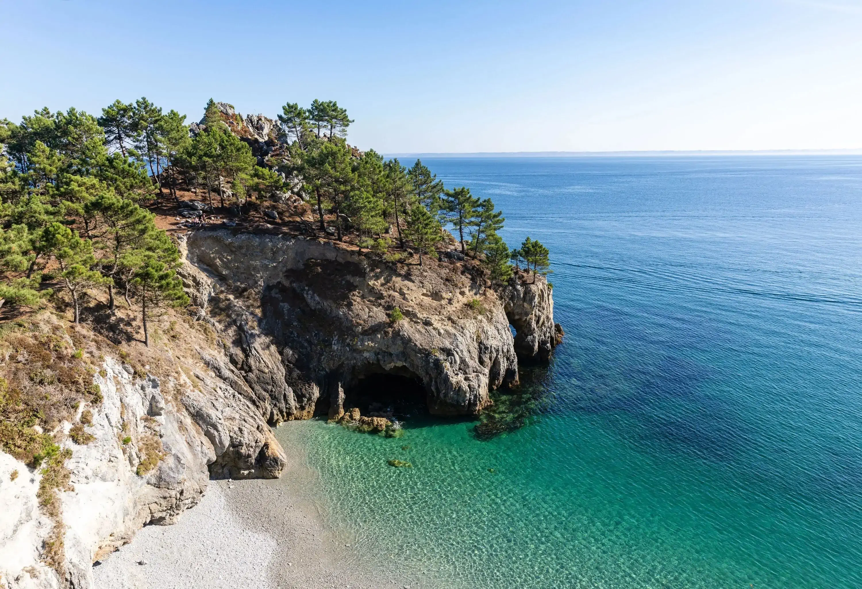 A rock cliff covered in trees overlooking a beach with turquoise waters.