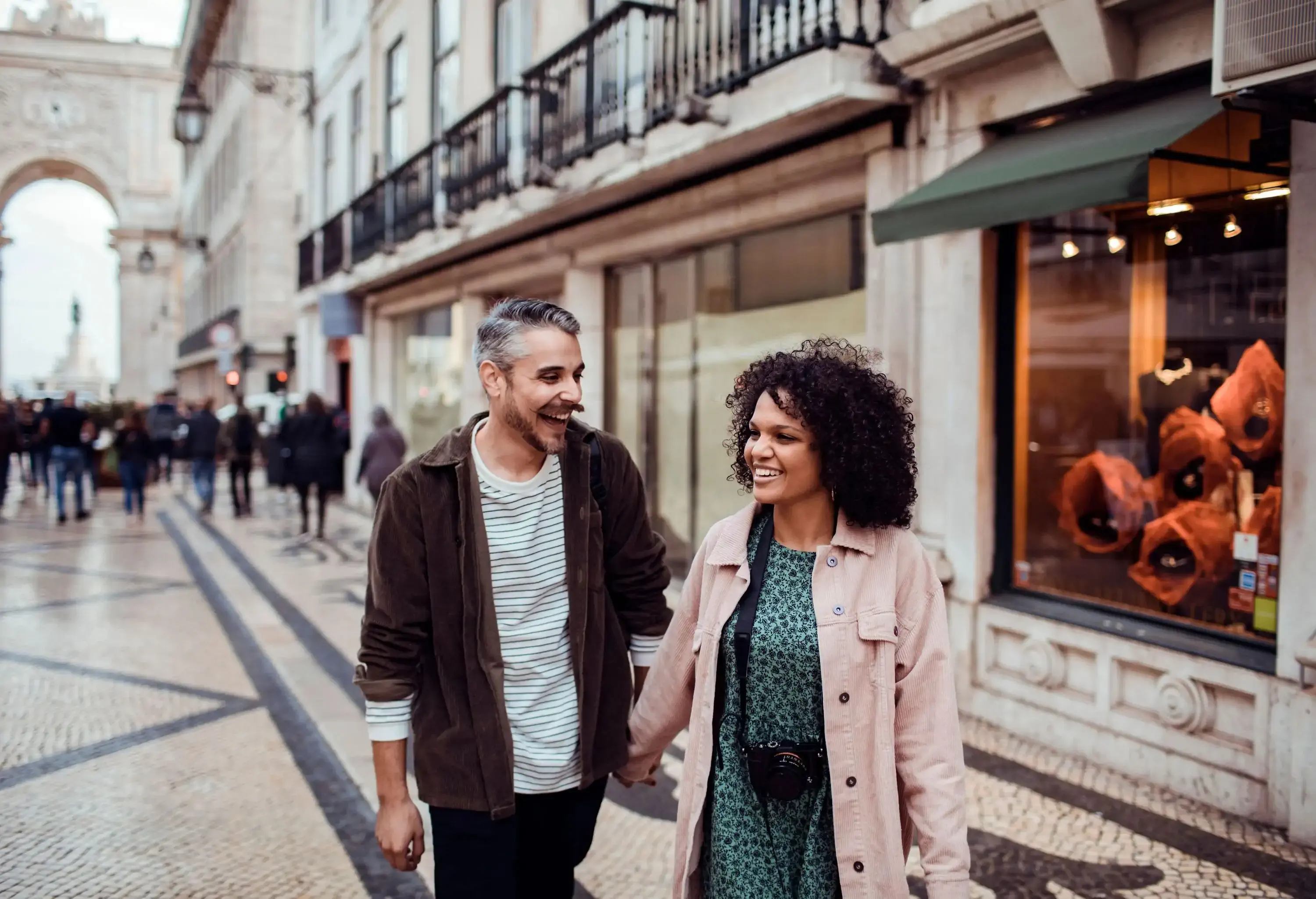 A happy couple holding hands while strolling down a shopping strip.