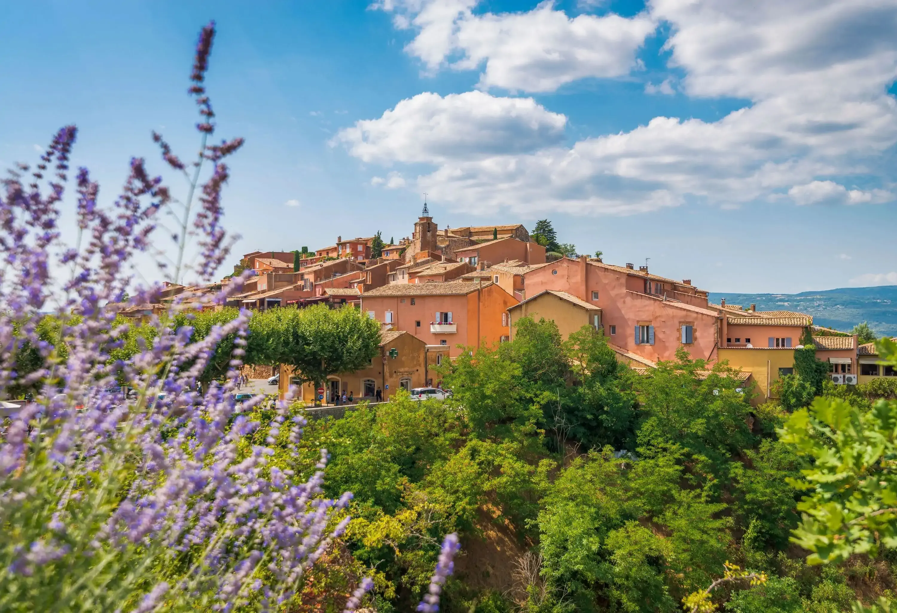 An ancient town perched on a green hill against a cloudy blue sky.
