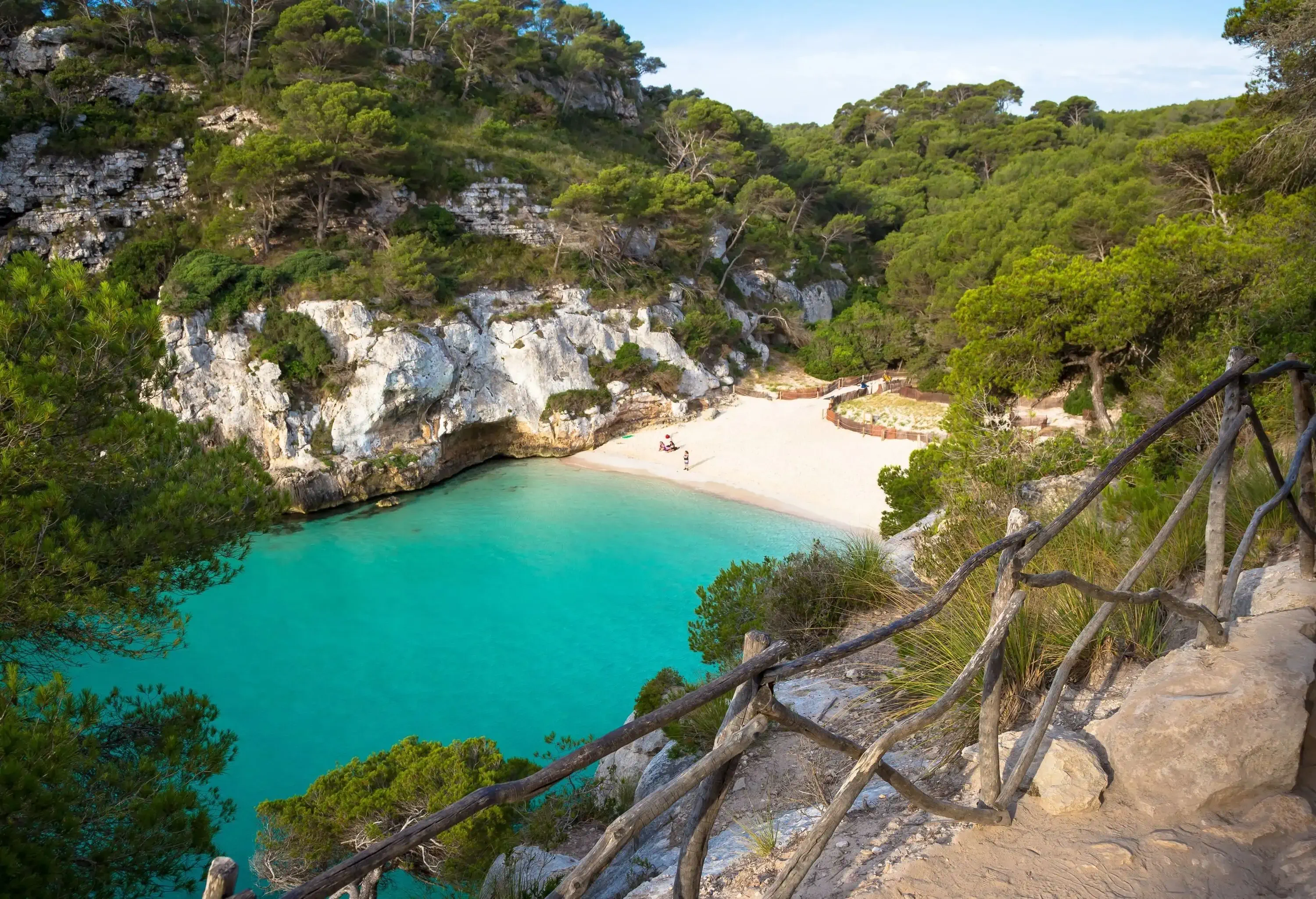 Turquoise waters of the sea against white sand beach surrounded by forested cliffs.