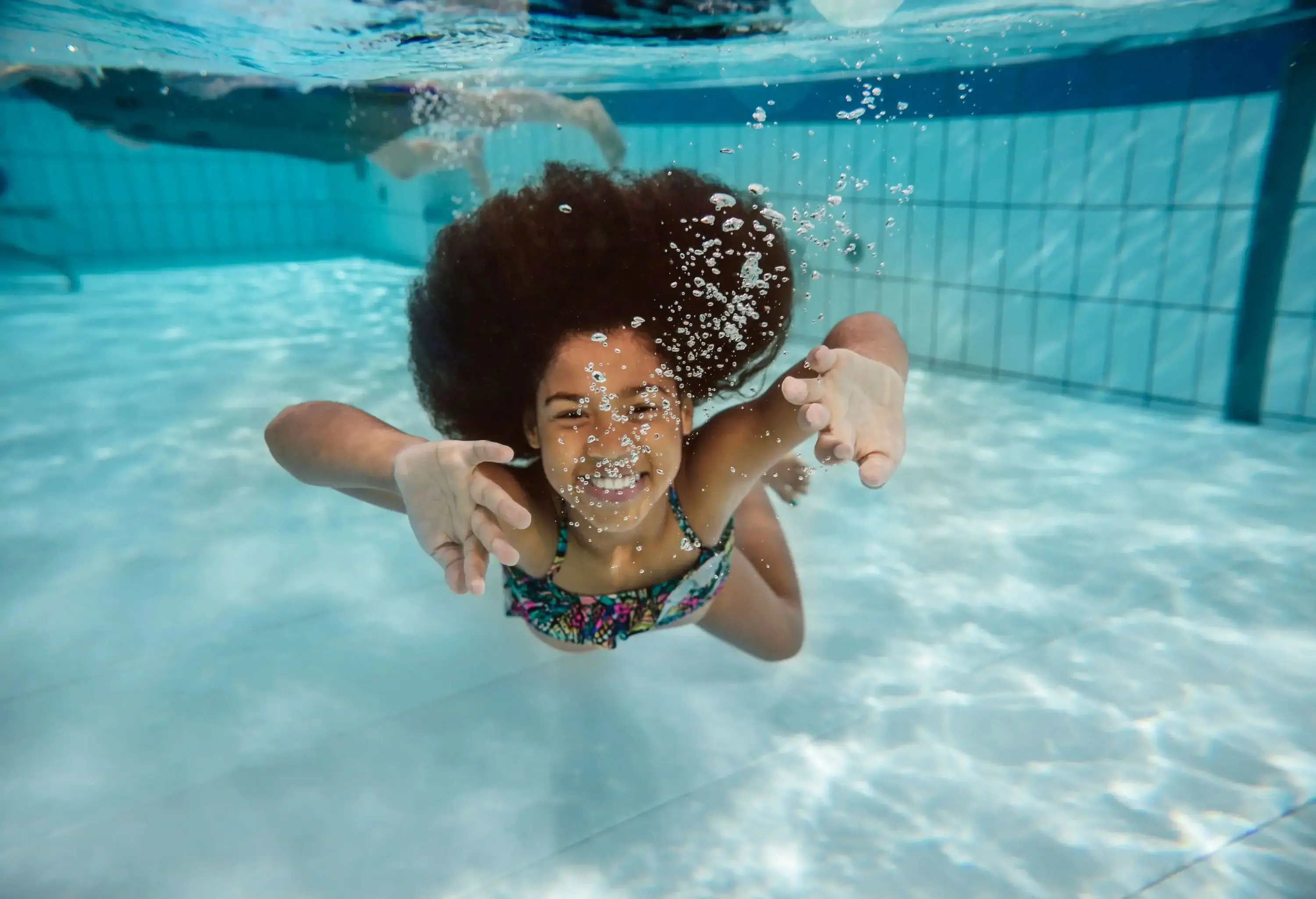 A girl dives under the swimming pool blowing bubbles in her mouth.