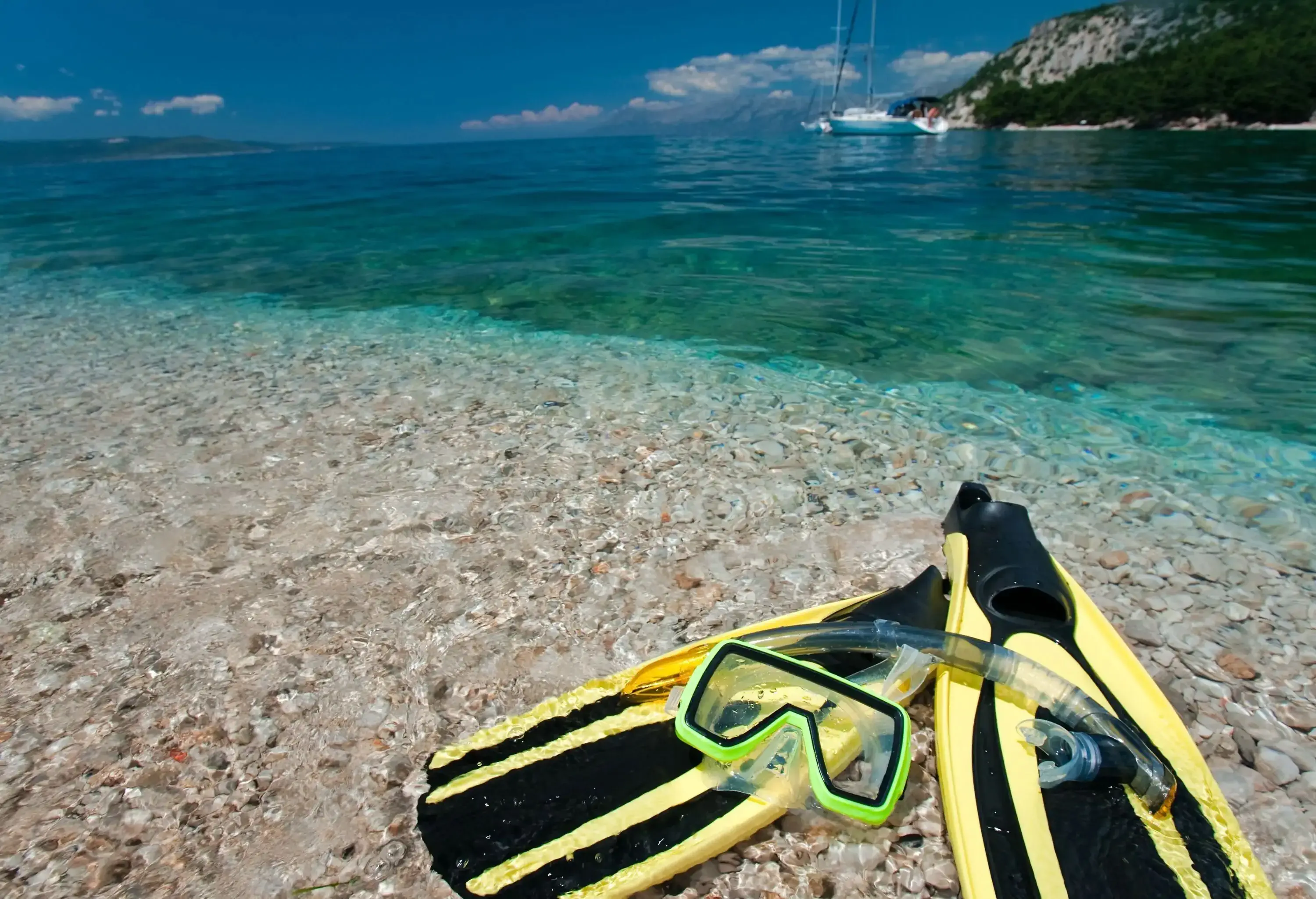 A snorkel mask and fins left on a rocky shore with crystal clear waters.