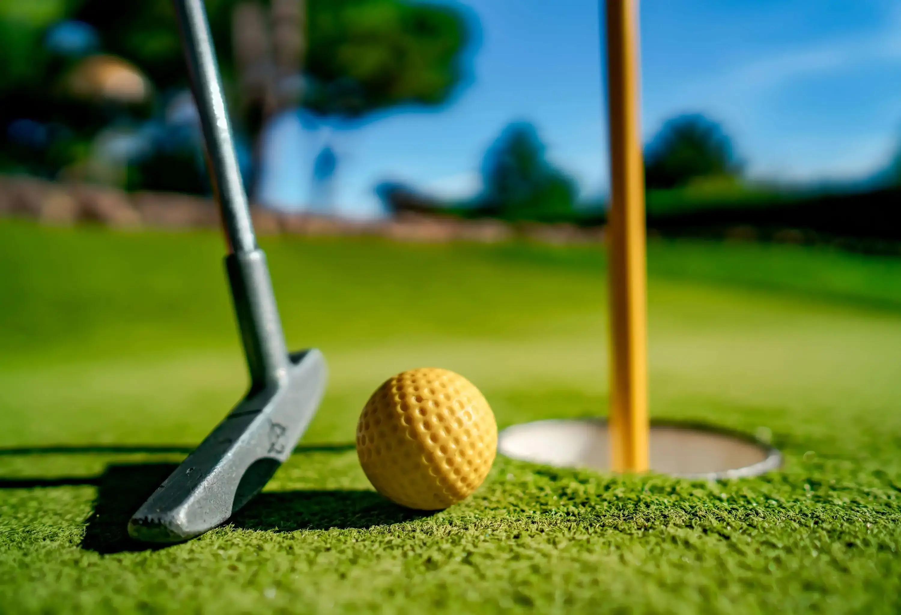 A yellow golf ball and a golf bat are near the hole.