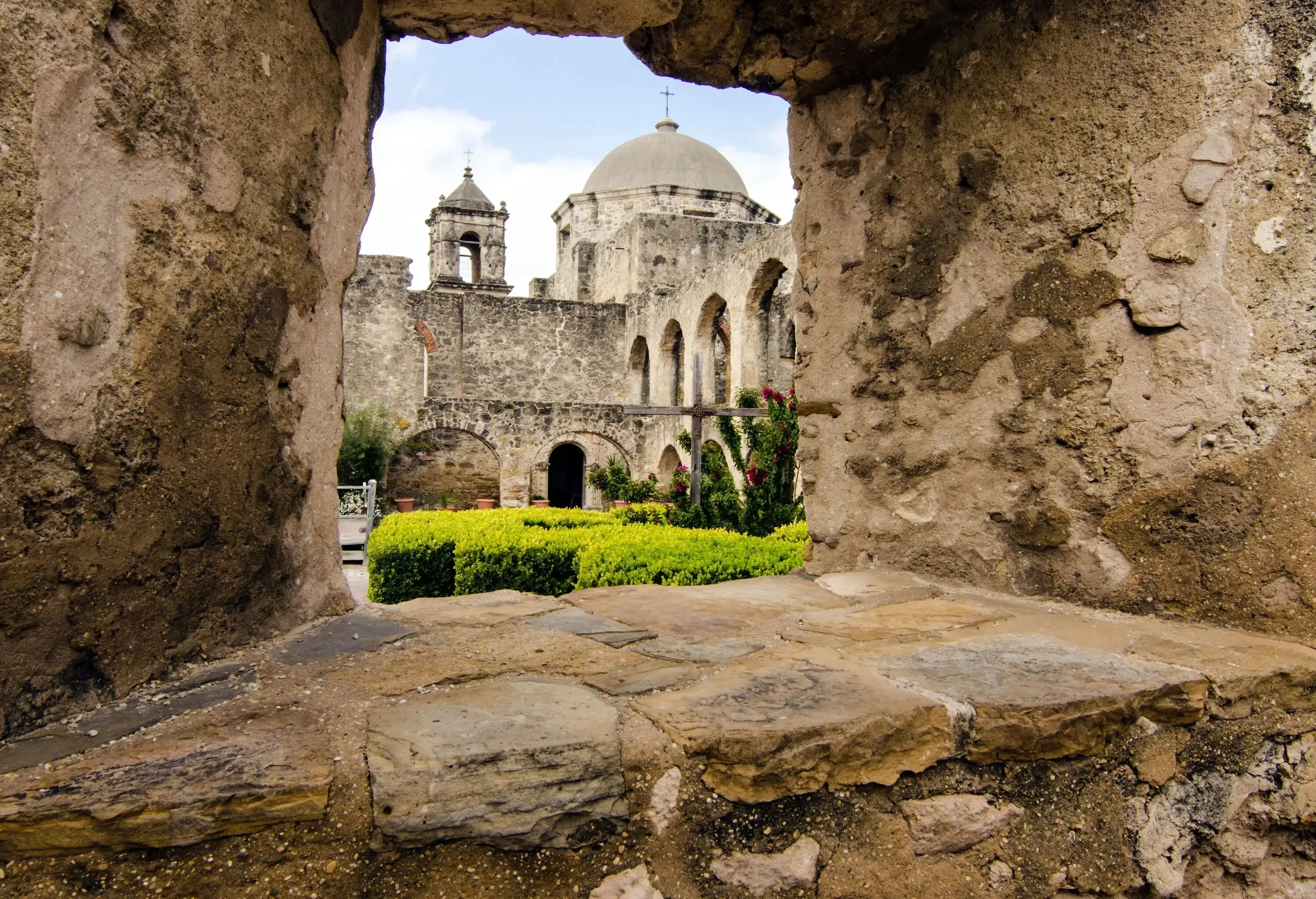 A view of San Jose Mission is framed through a weathered stone window, showcasing the architectural beauty and rich history of the site.