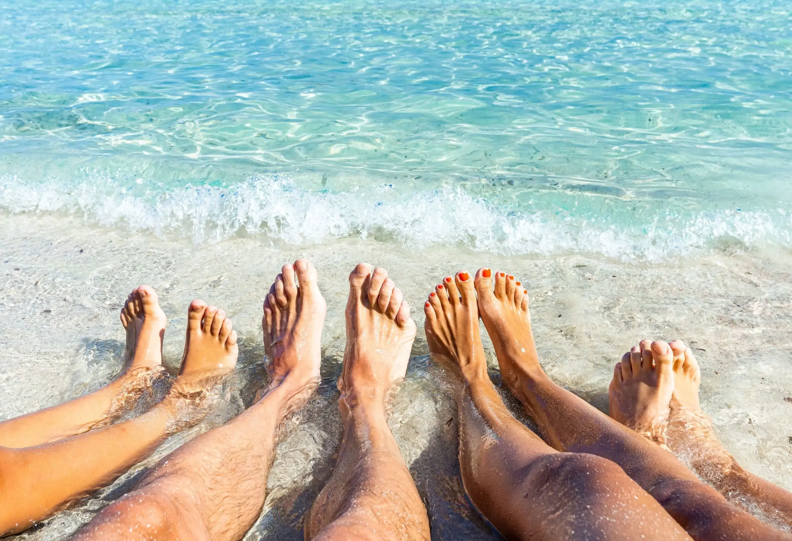 Four people barefoot feet on the shore on the beach.
