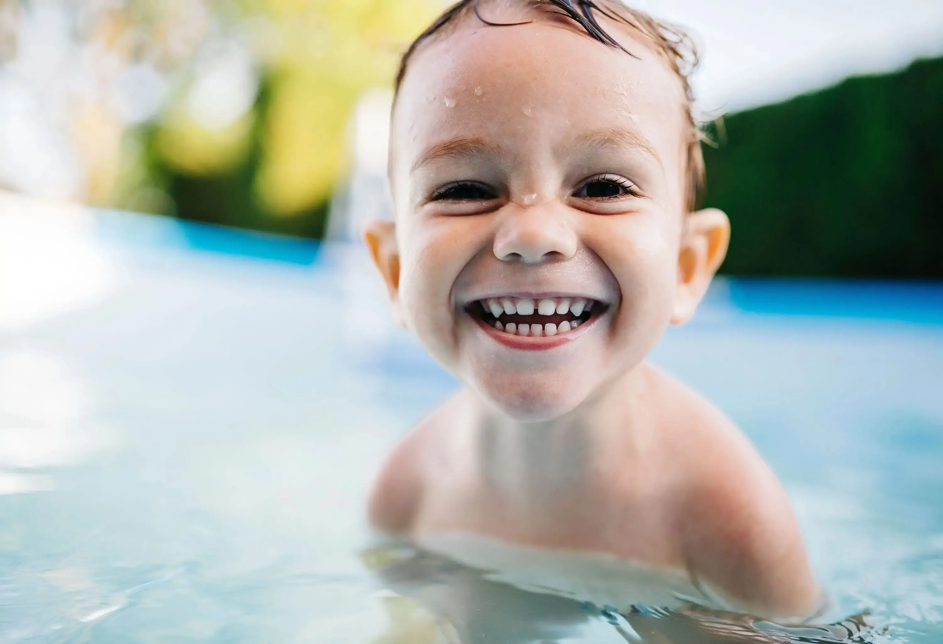 A portrait of a young, happy boy is seen in a small pool filled with water.