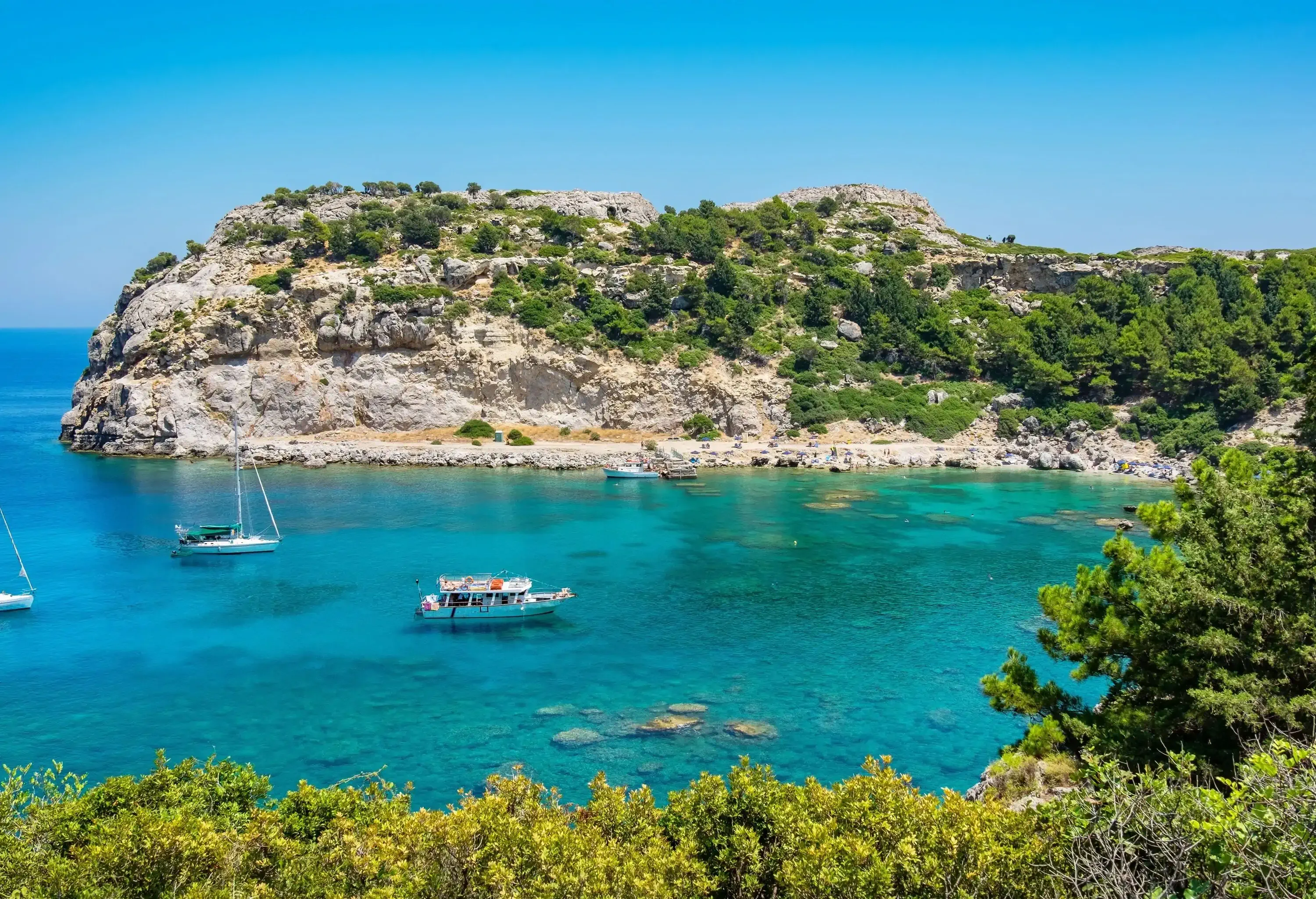 Three boats anchor in a scenic bay embraced by rugged rock formations adorned with lush foliage.