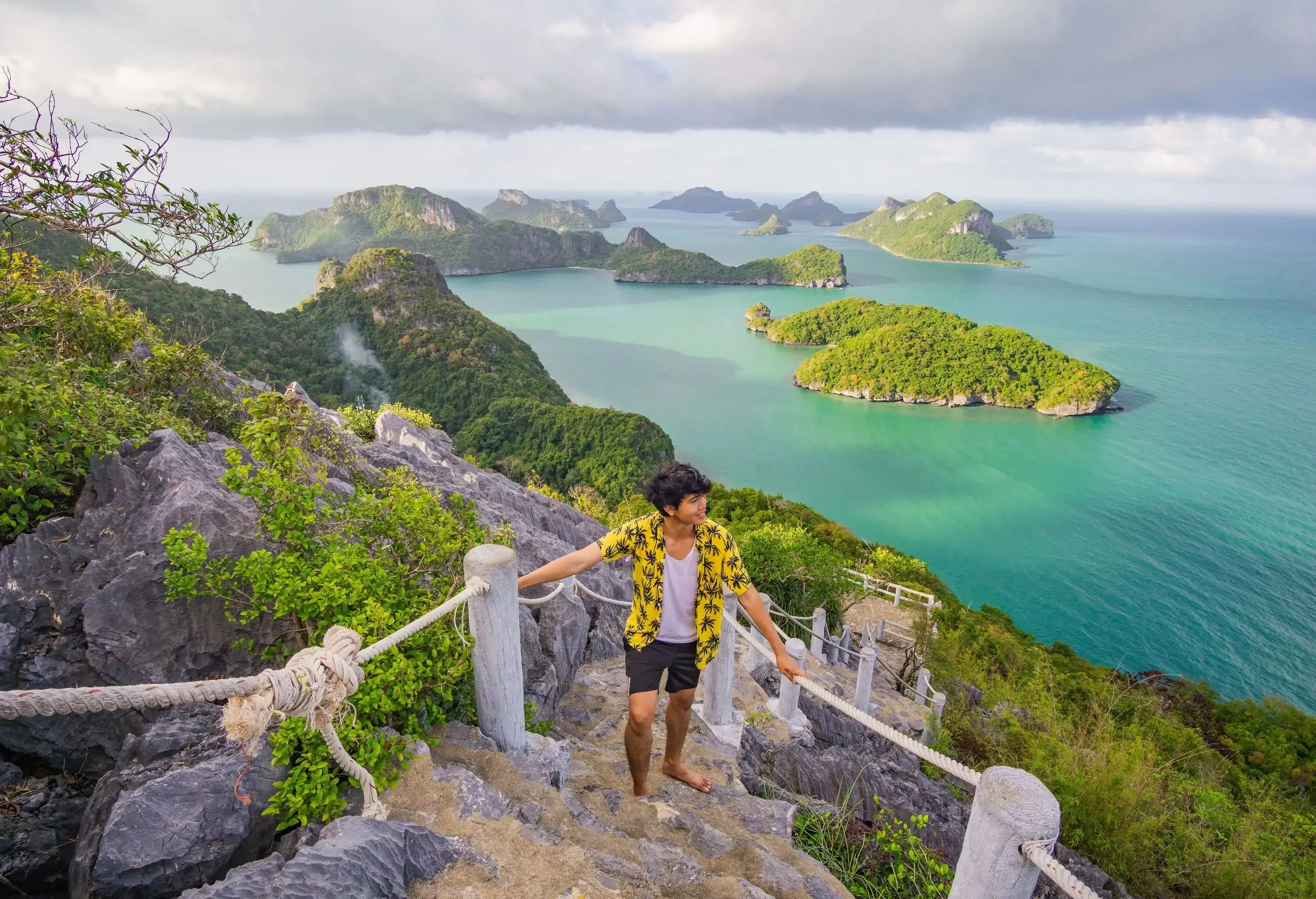 A man stands on a stairway with a view of the mountains below, the emerald sea