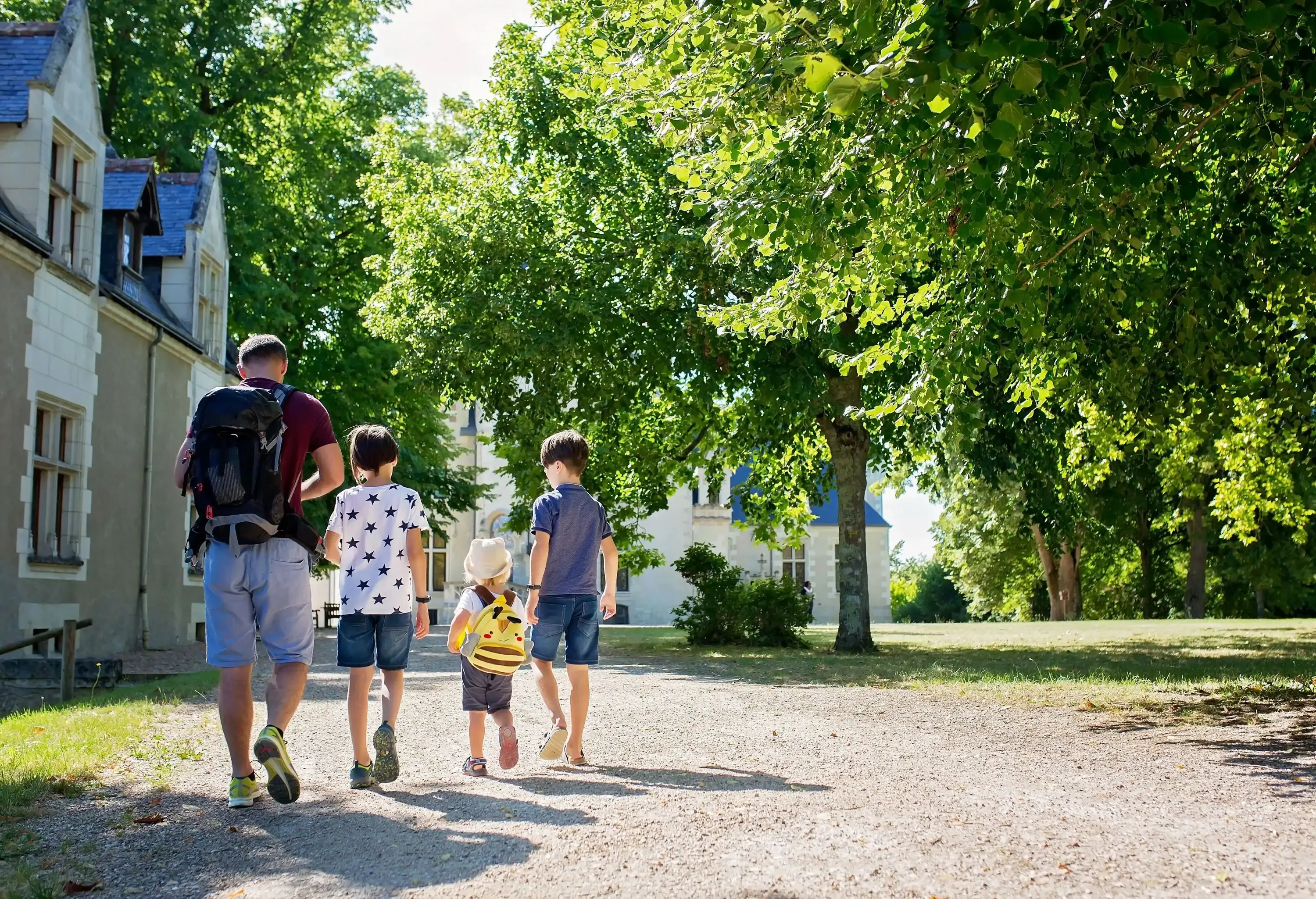 A father with three children walking together in the lush park with tall green trees.