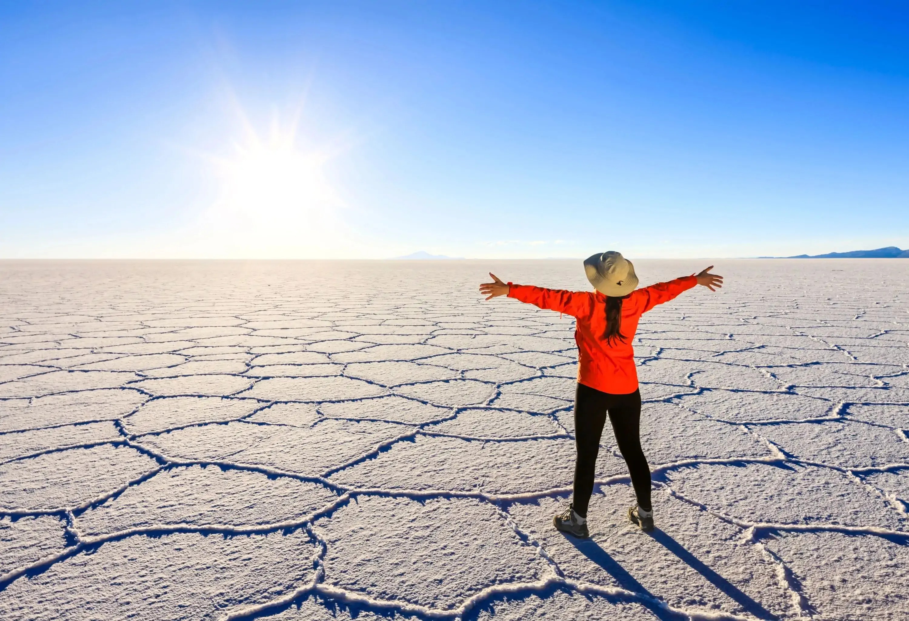 A woman standing on hardened salt pans with her arms outstretched, soaking up the bright sunlight.