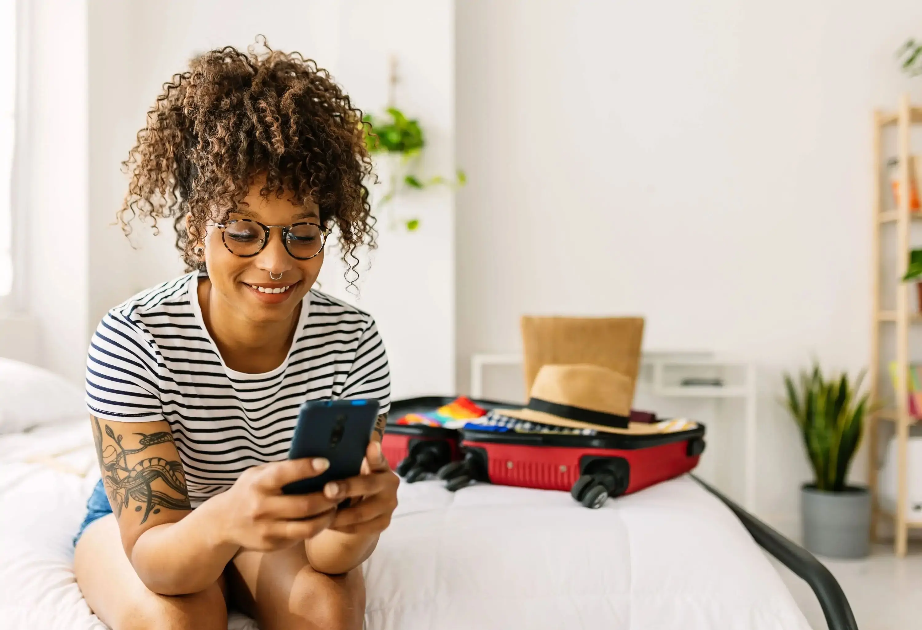 A woman sitting on a bed with her smartphone and trying to make a reservation