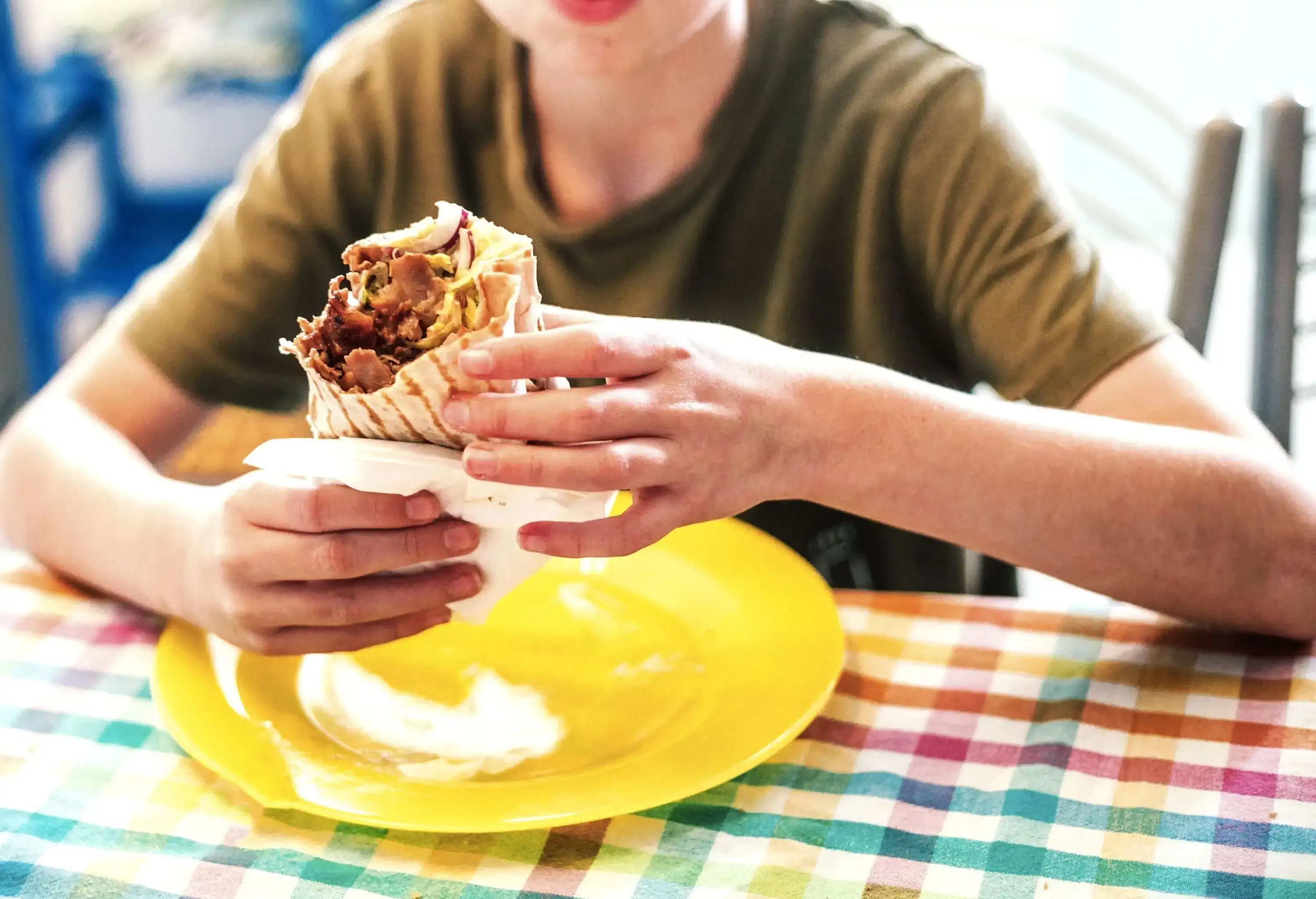 A young kid eating shawarma served on a bright yellow plate.