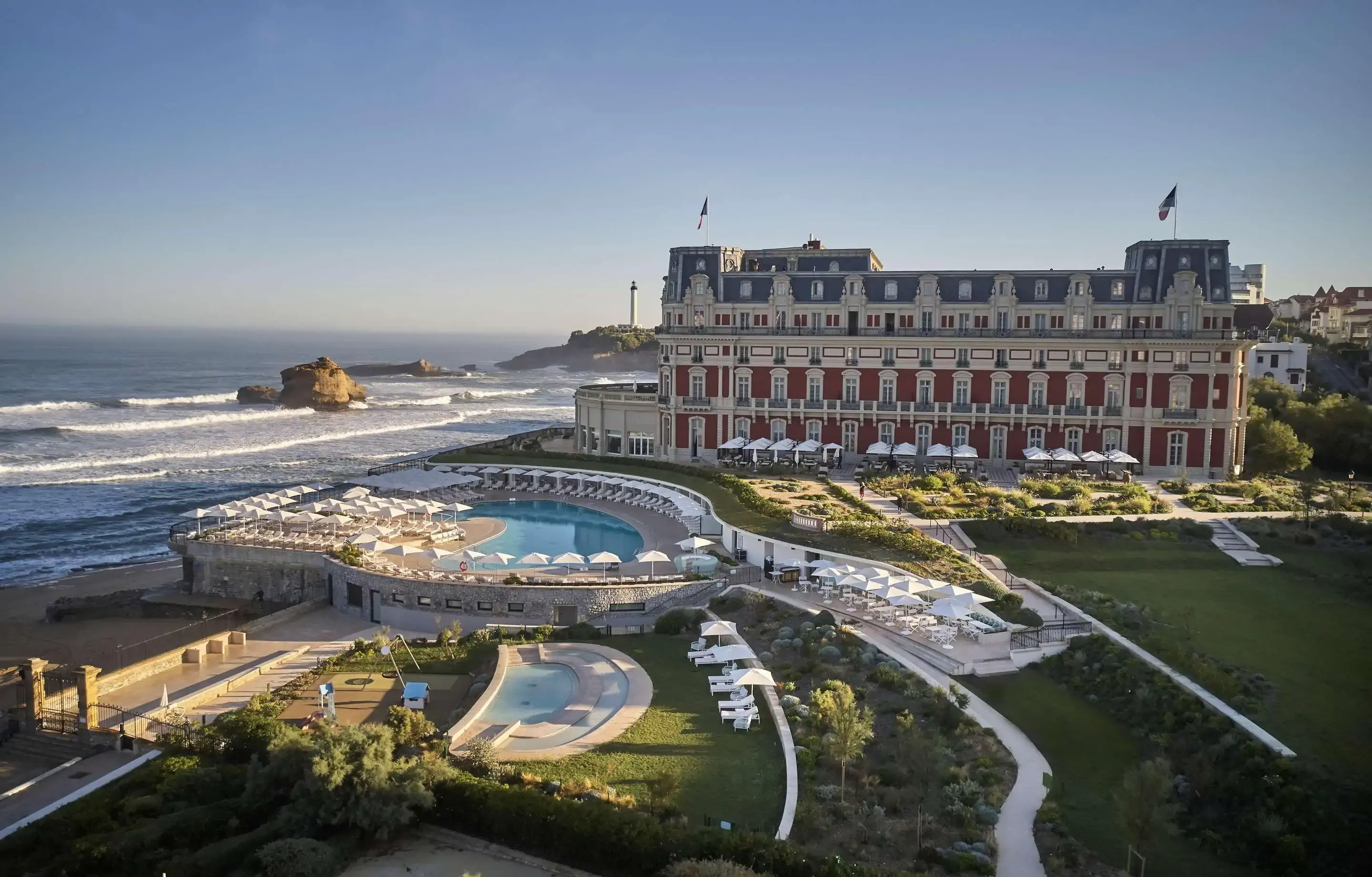 Aerial view of a large hotel built by the beach with swimming pools and green lawns