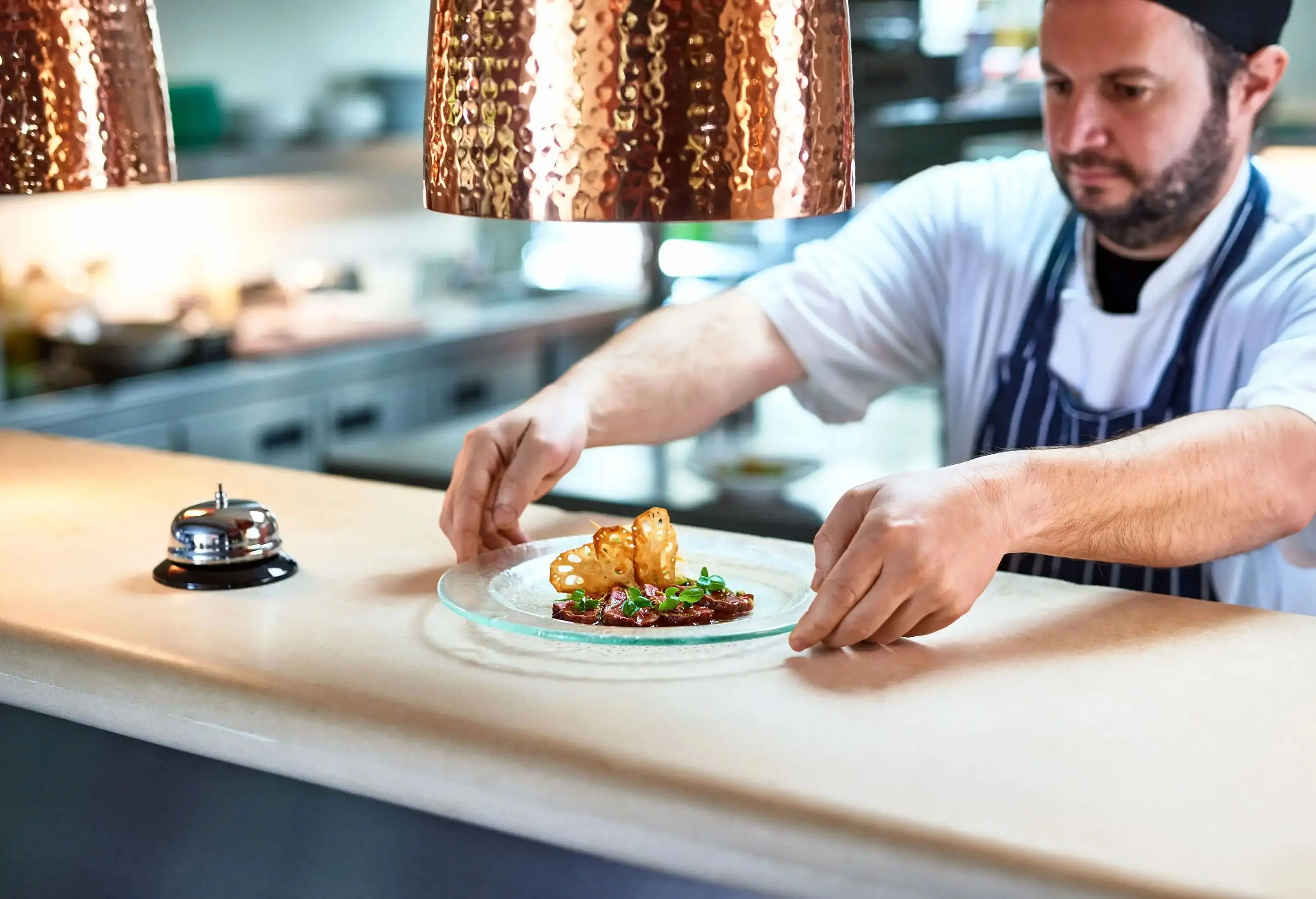 A chef places a gourmet dish on the pass for servers to pick up.