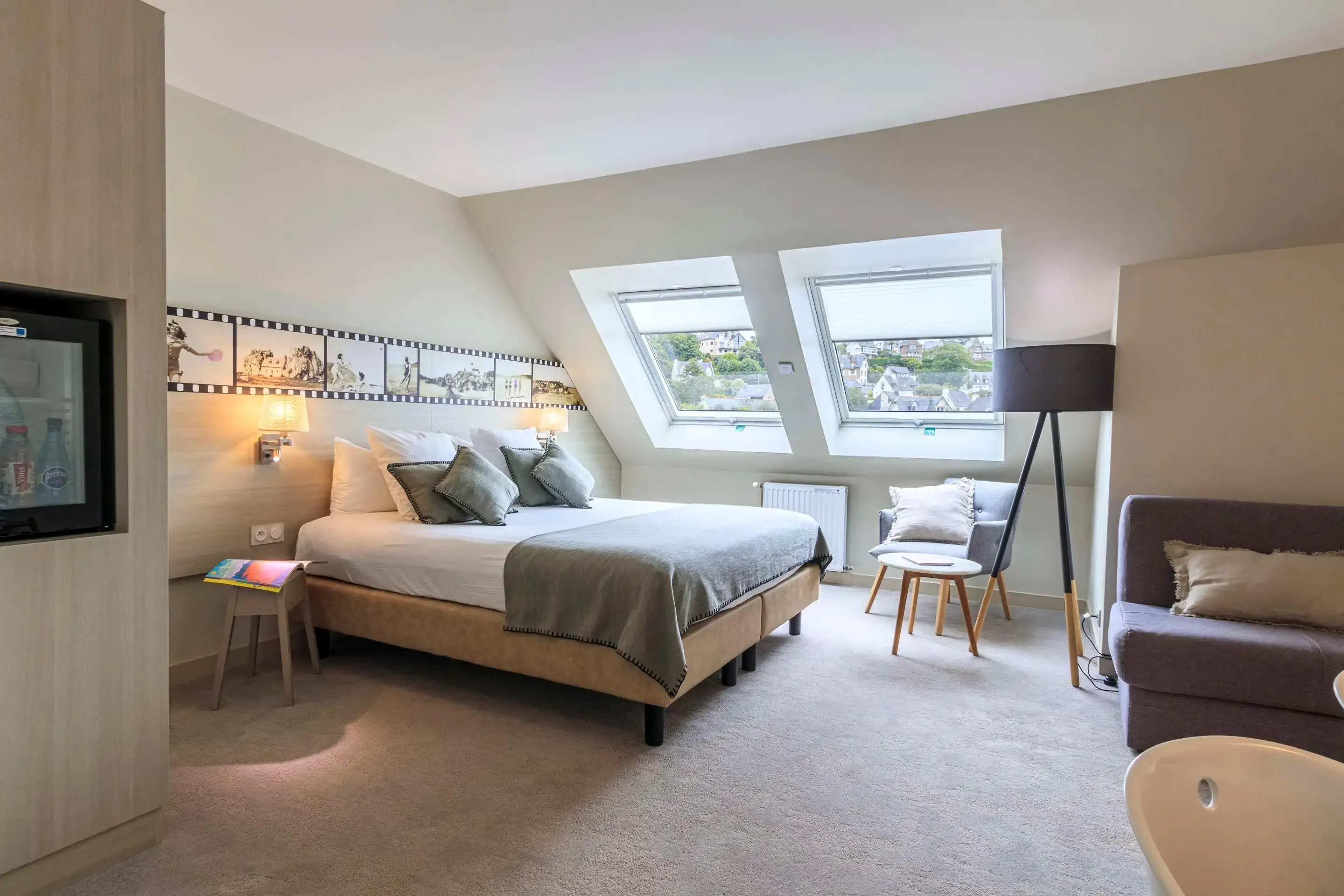 A modern hotel room with white carpet, movie pictures and two windows overlooking an old village