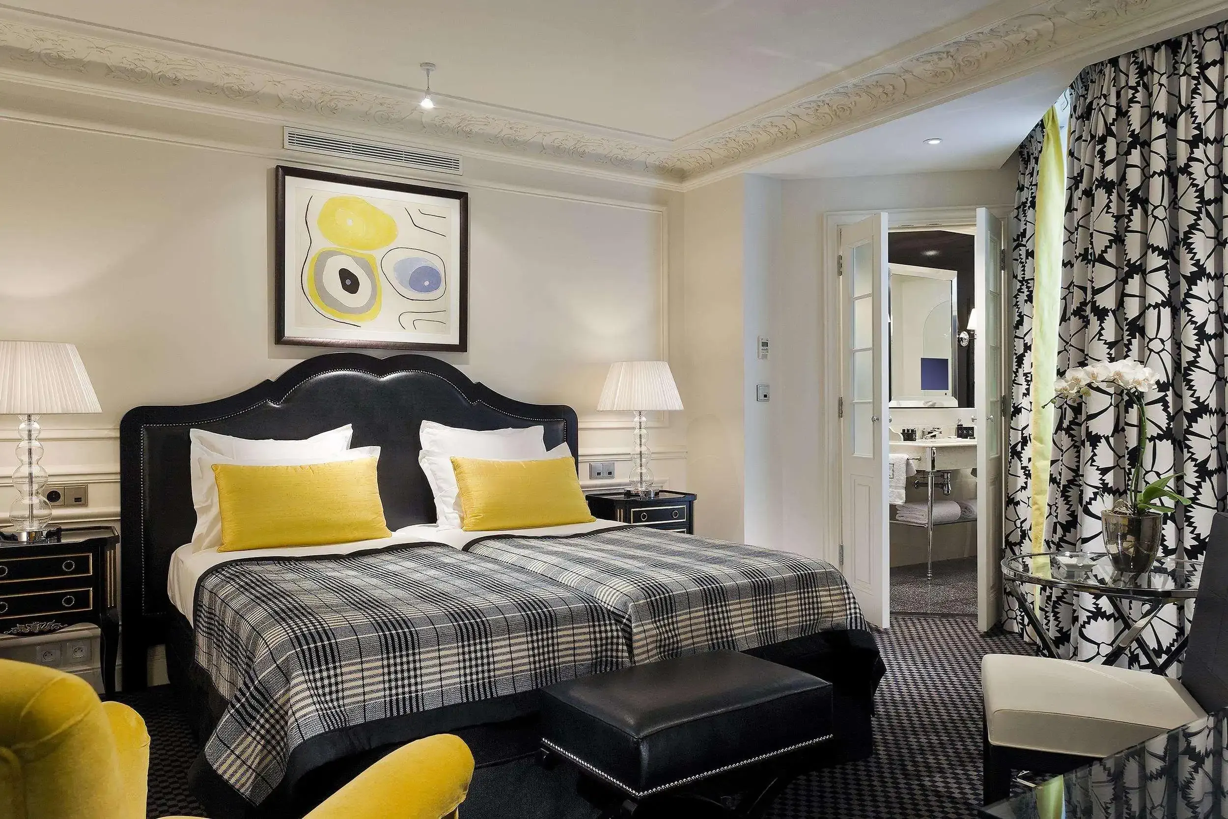 Luxury hotel room with view of a double bed with yellow cushions and view into the bathroom