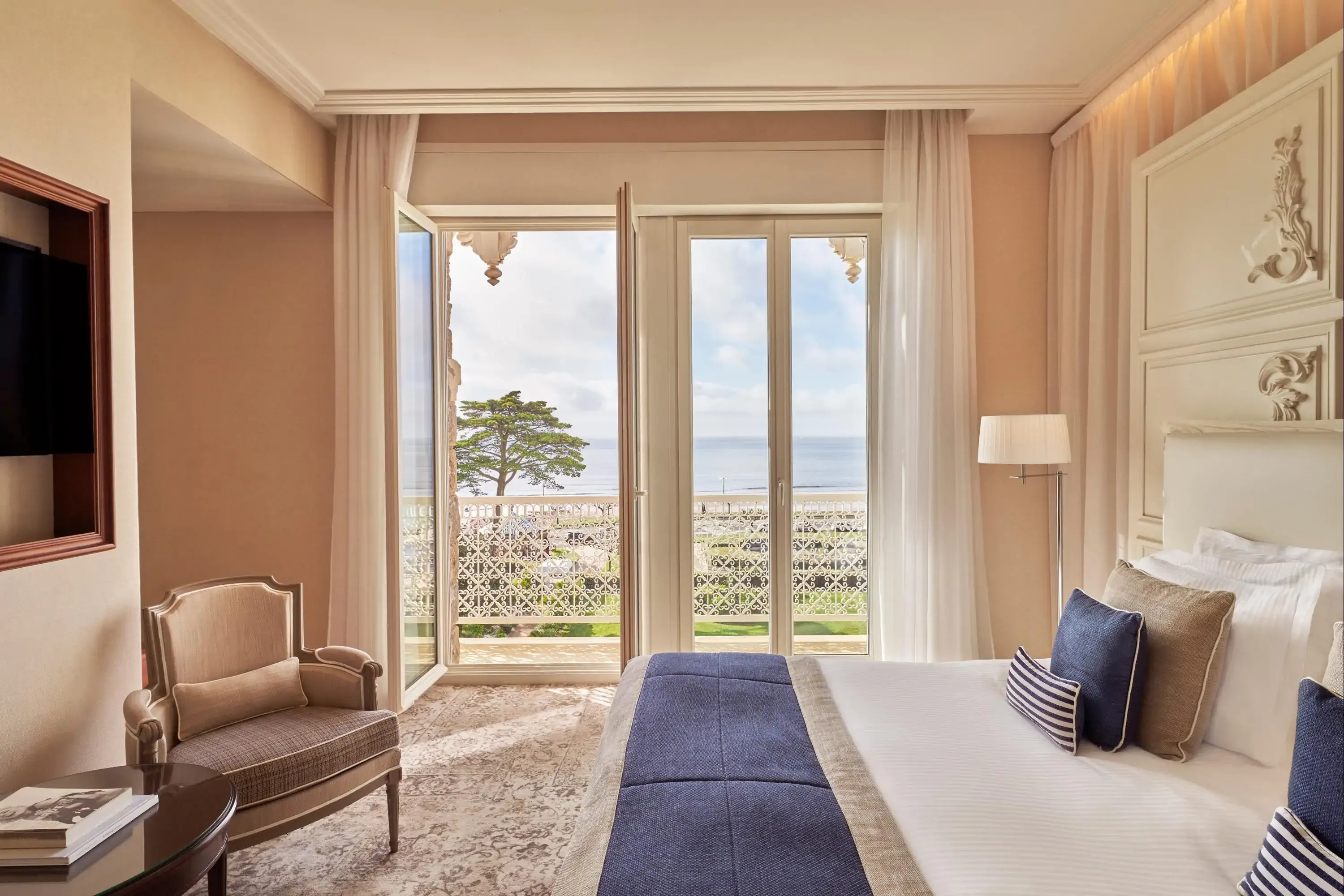 A hotel room with a double bed and a window opened to a balcony overlooking a beach