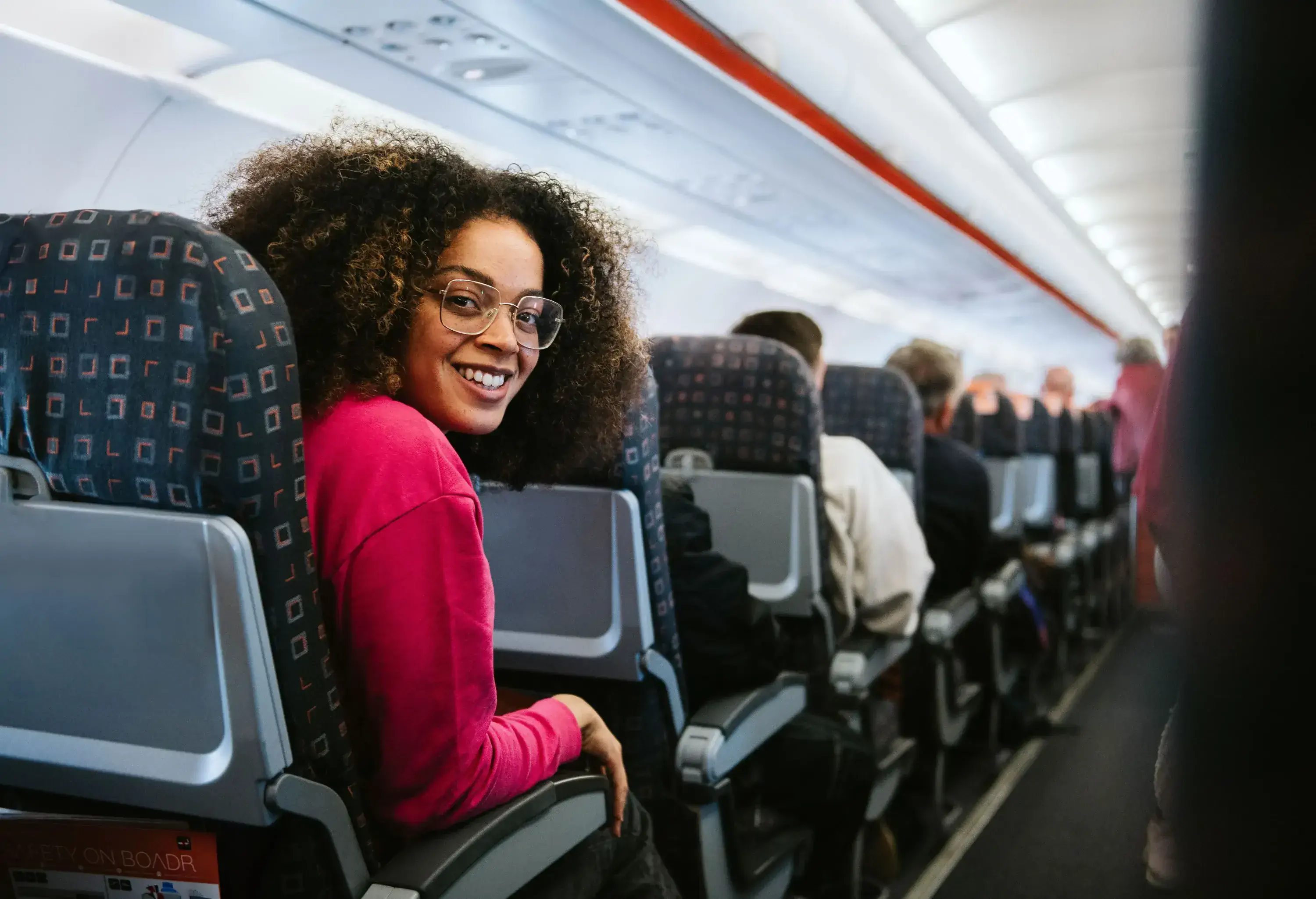 A smiling young woman looks over her shoulder from an airplane seat.