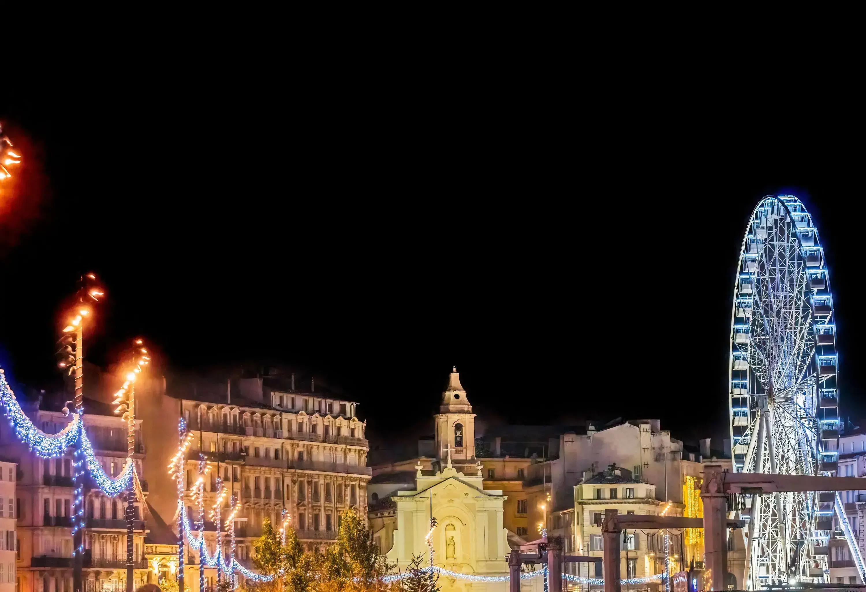 A dense collection of buildings framed by vibrant Christmas lights and a glowing Ferris wheel.