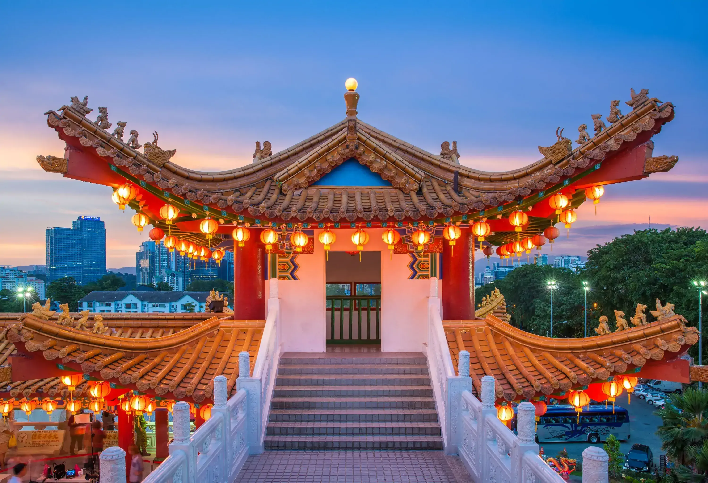 A colourful Chinese temple with illuminated lanterns and a cityscape in the background.