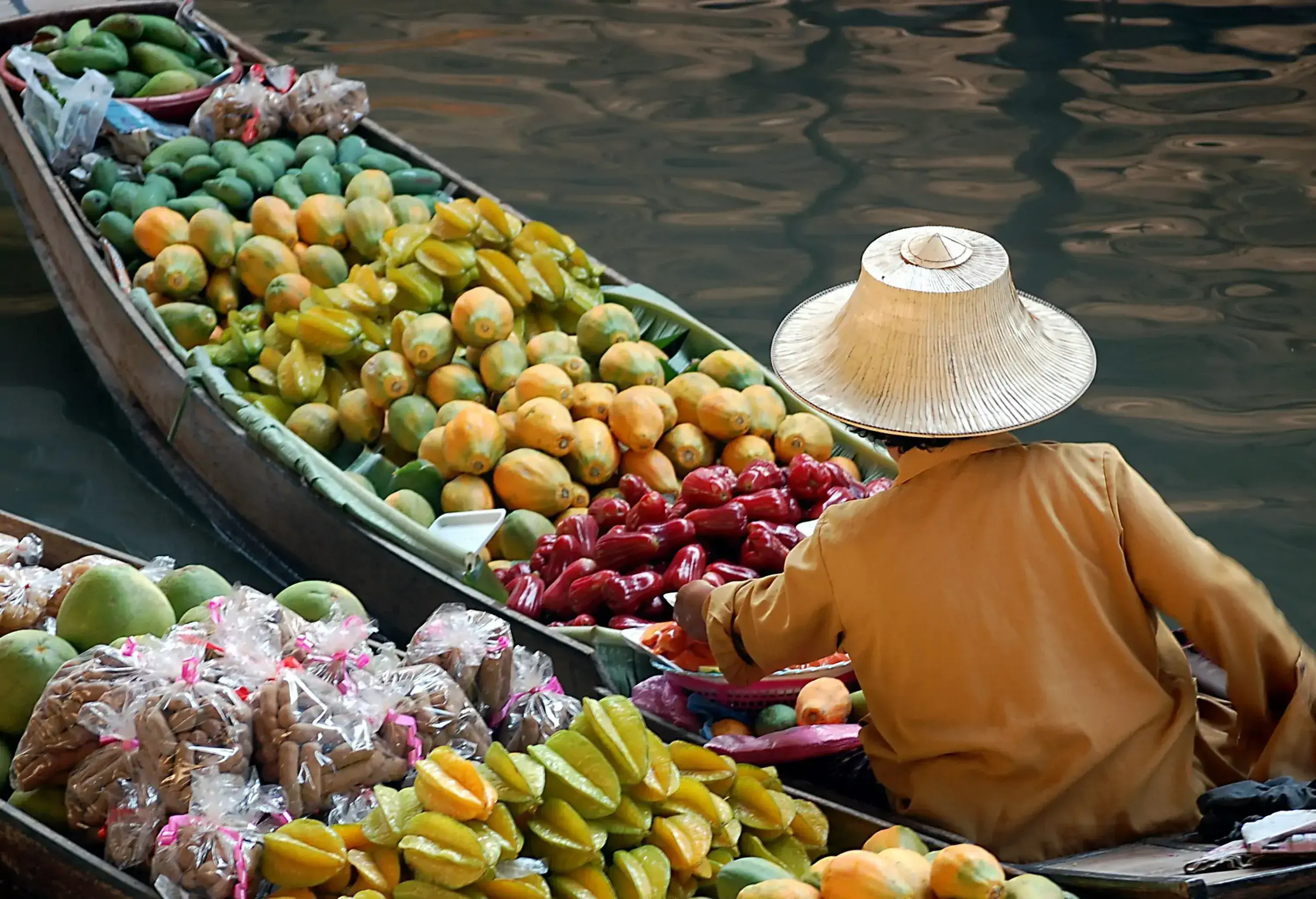 An individual on a boat filled with various fruits and vegetables at the traditional floating market.