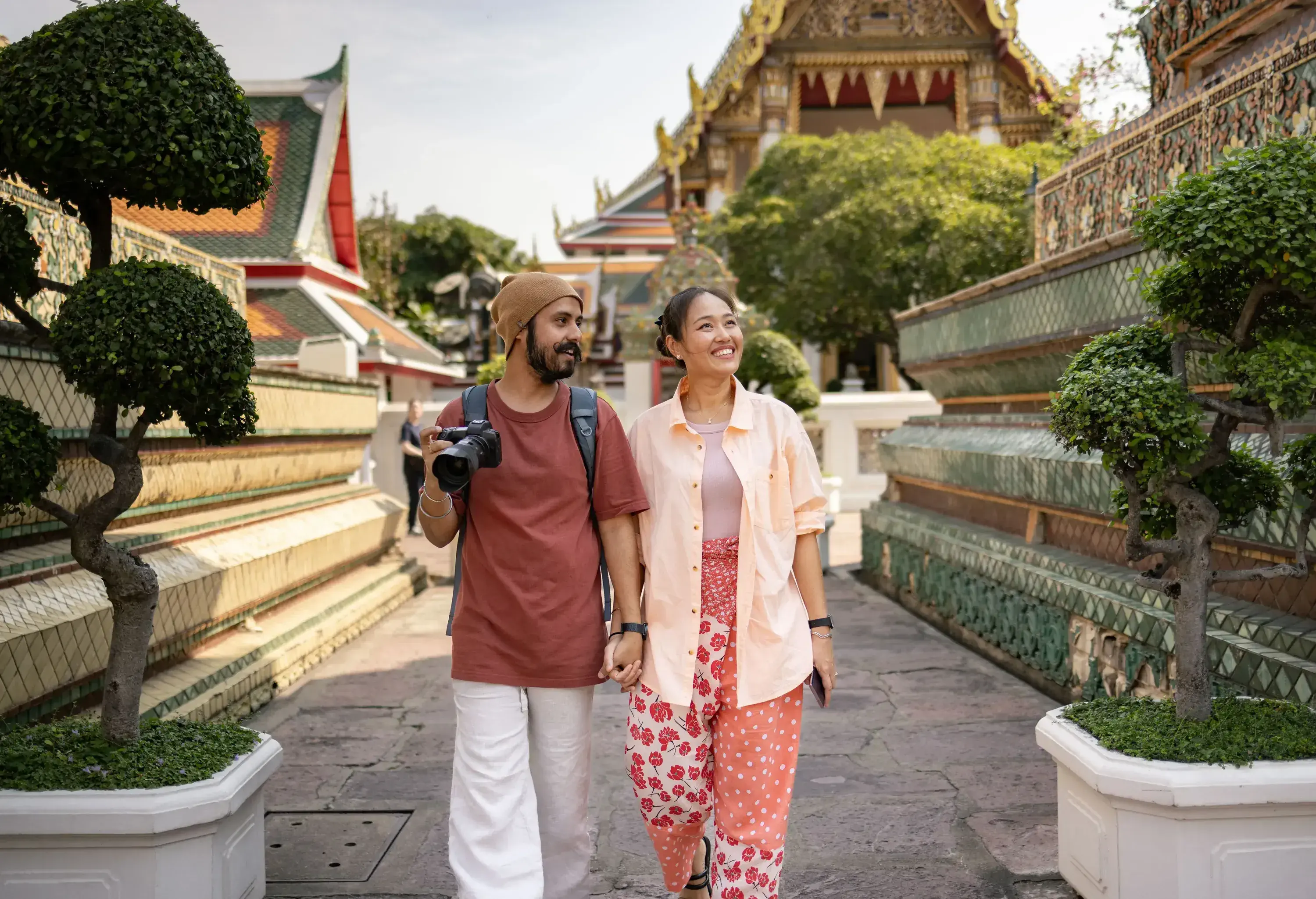 A smiling couple hold hands while walking through an ornate temple complex.