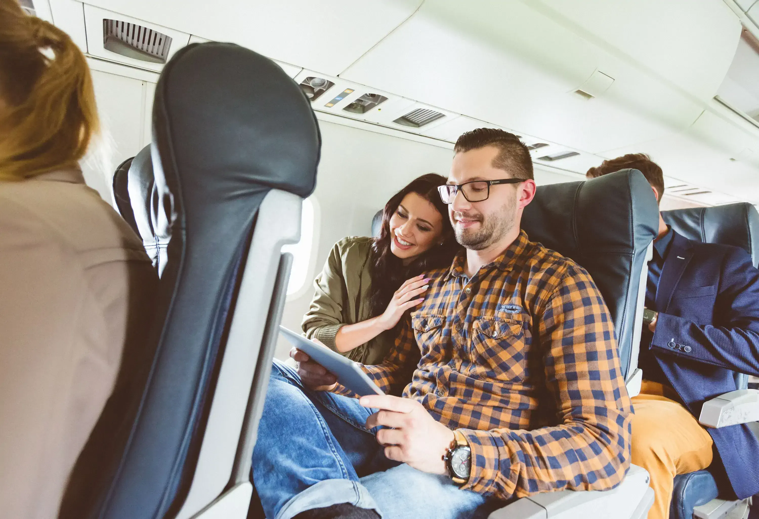 Happy young people traveling by airplane using digital tablet. Couple flying by plane using tablet pc.