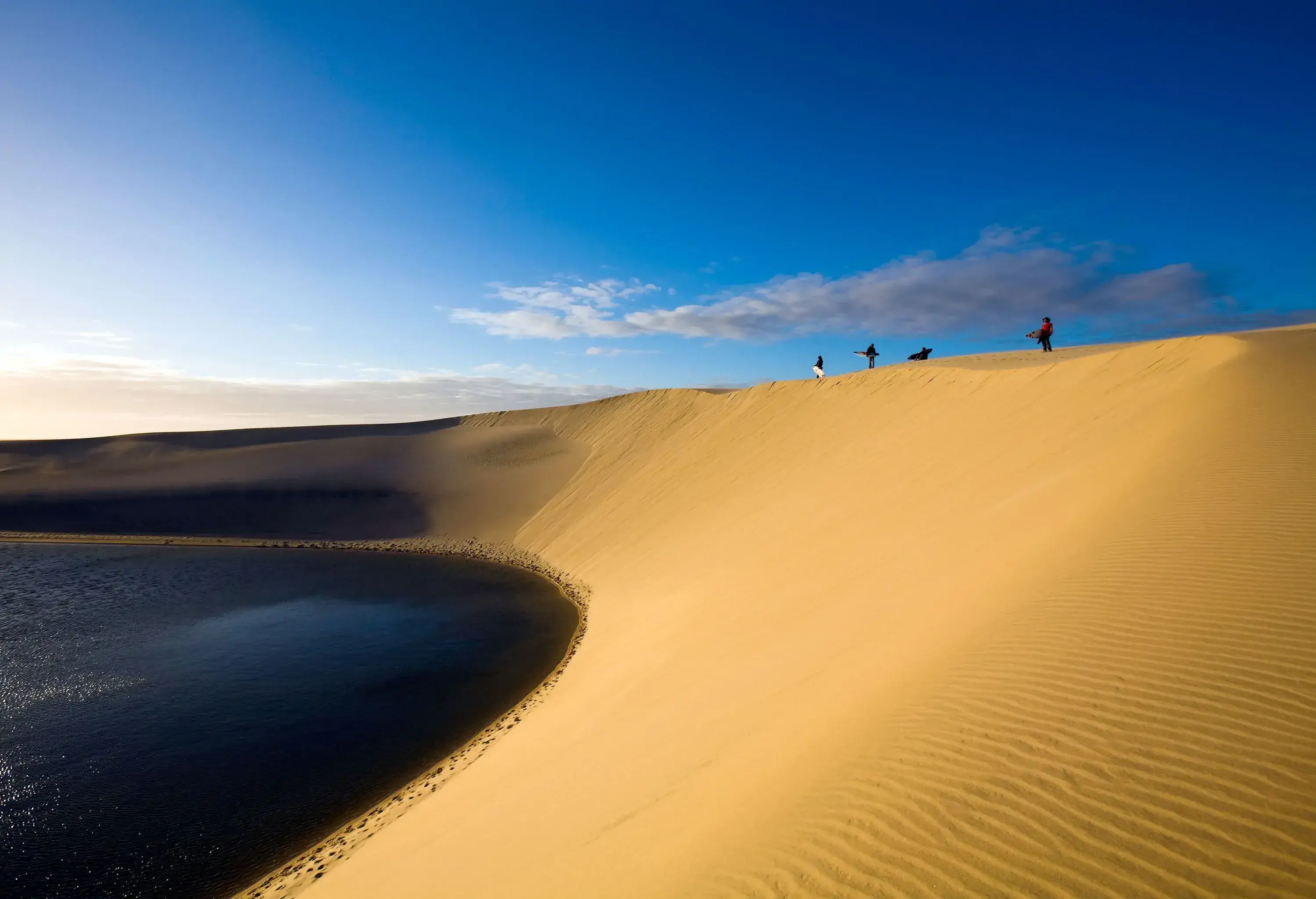 Tourists standing at the edge of the sand cliff surrounding the tranquil lake.