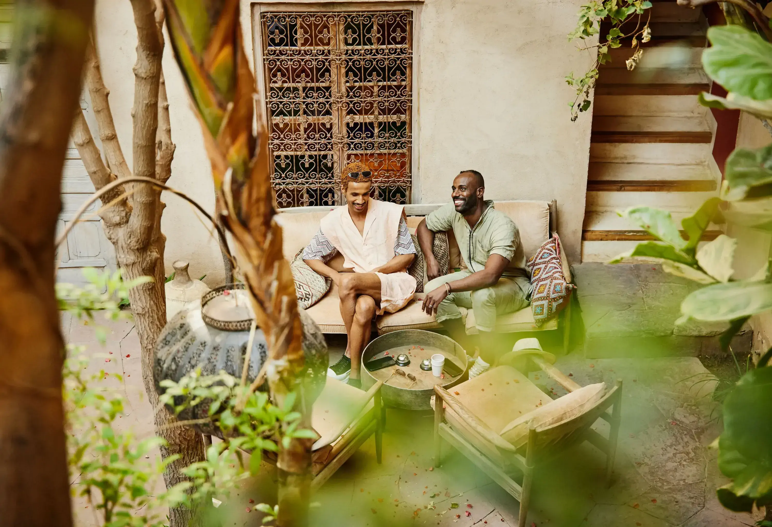 Wide shot high angle view of male friends sitting on couch in courtyard garden of riad while on vacation in Marrakech