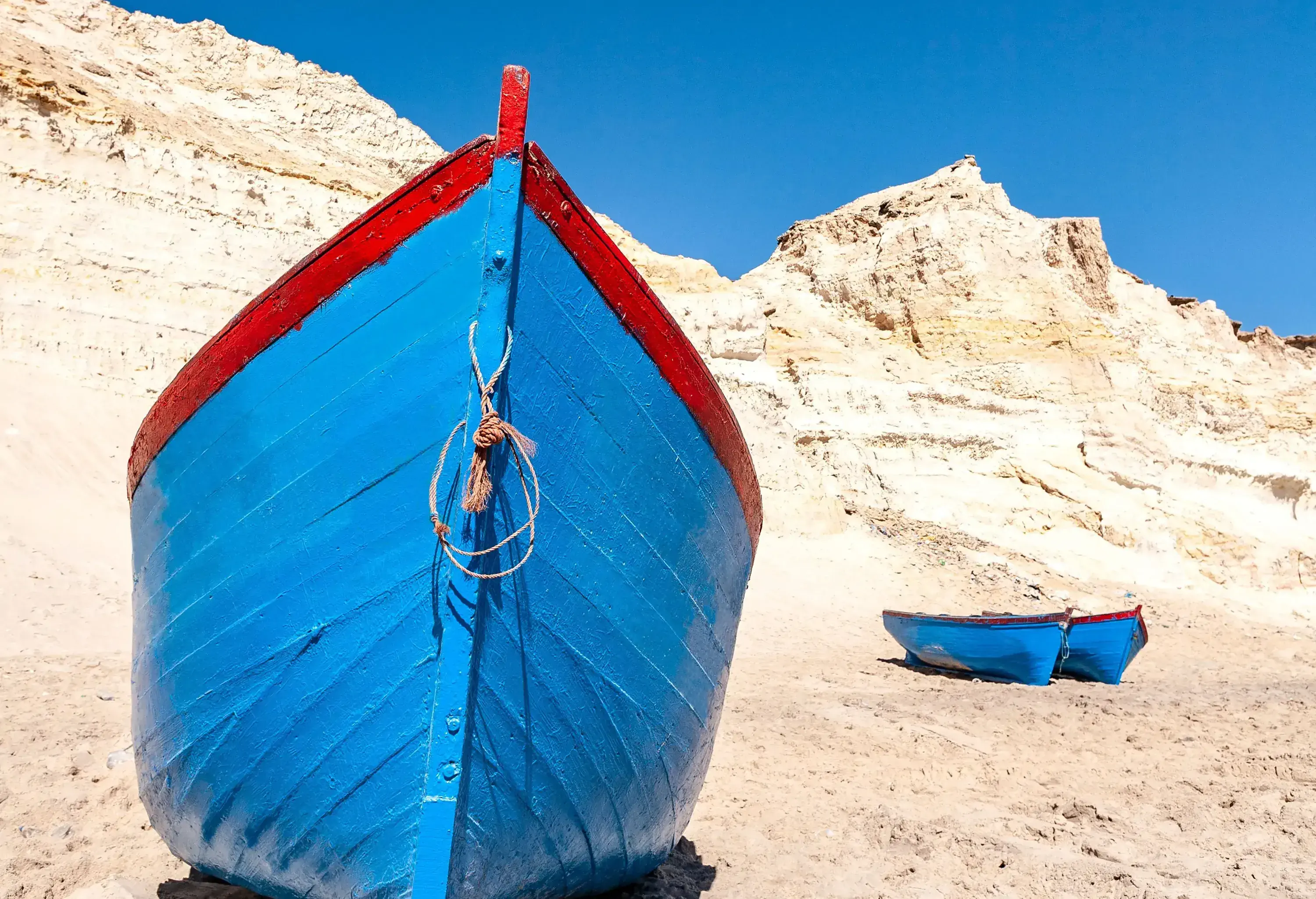 Three blue wooden fishing boats on a rocky shore.
