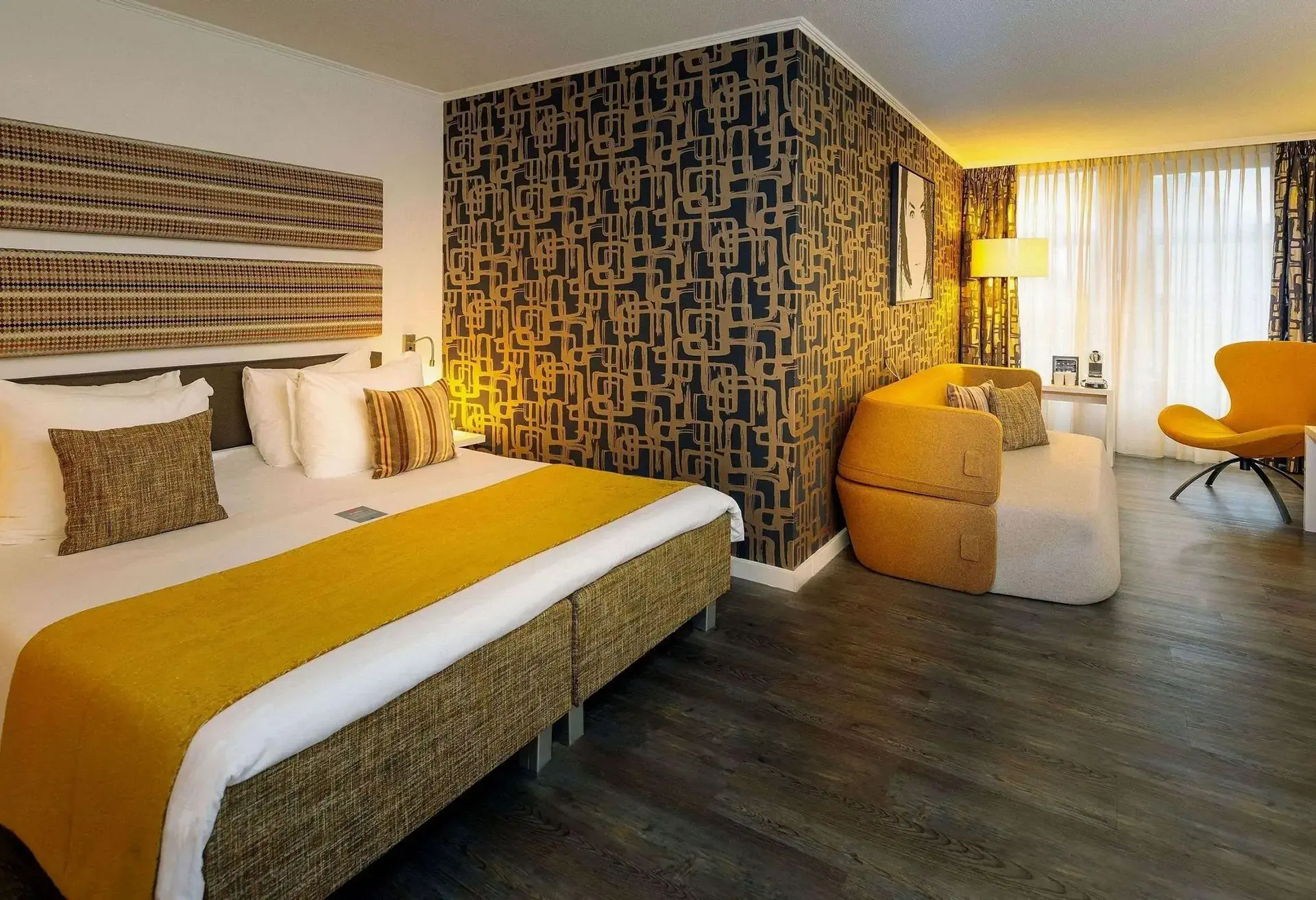 A hotel room decorated in 1960s style with patterned wallpaper, large bed and a sofa