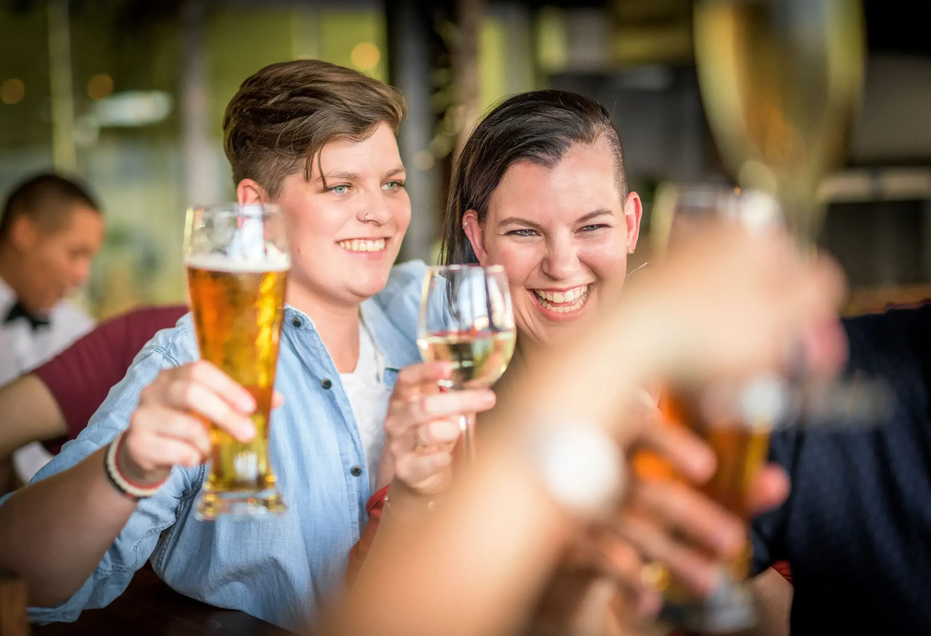 A female couple smiles as they raise their glasses to make a toast.