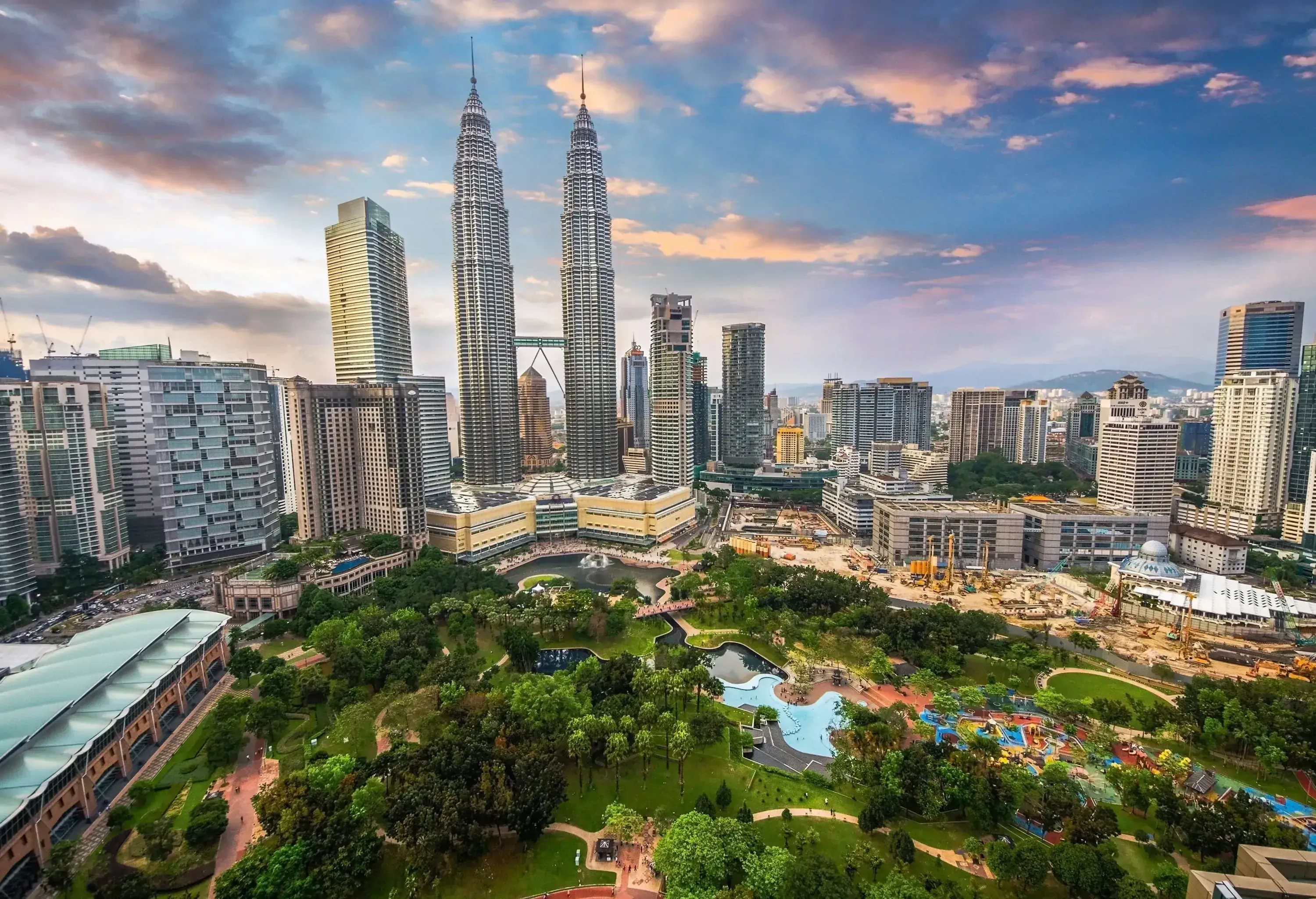 Lush trees frame a serene park in the foreground, as the iconic Petronas Towers rise proudly against the Kuala Lumpur city skyline in the background.