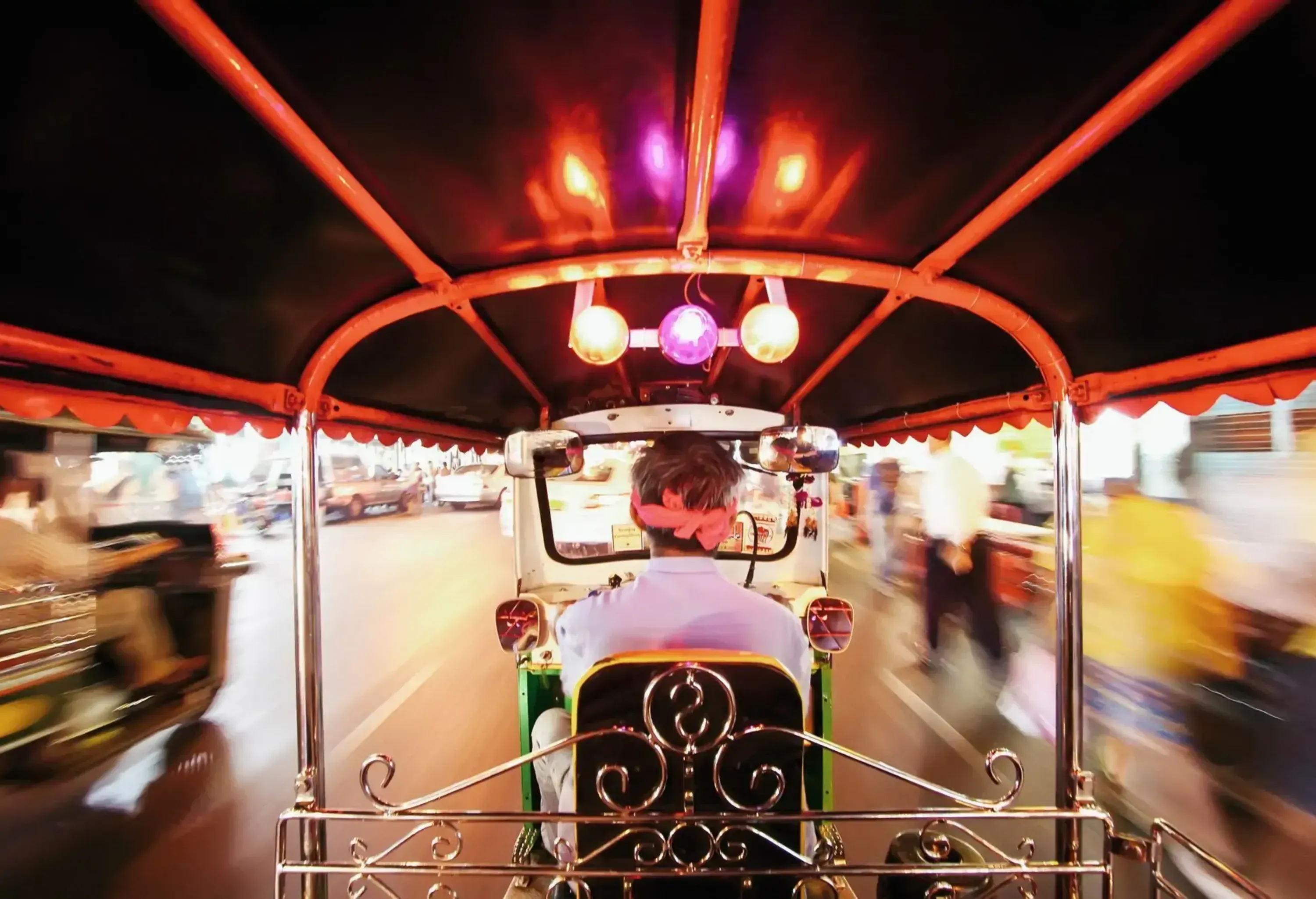 A Tuk Tuk travelling down the road at night.