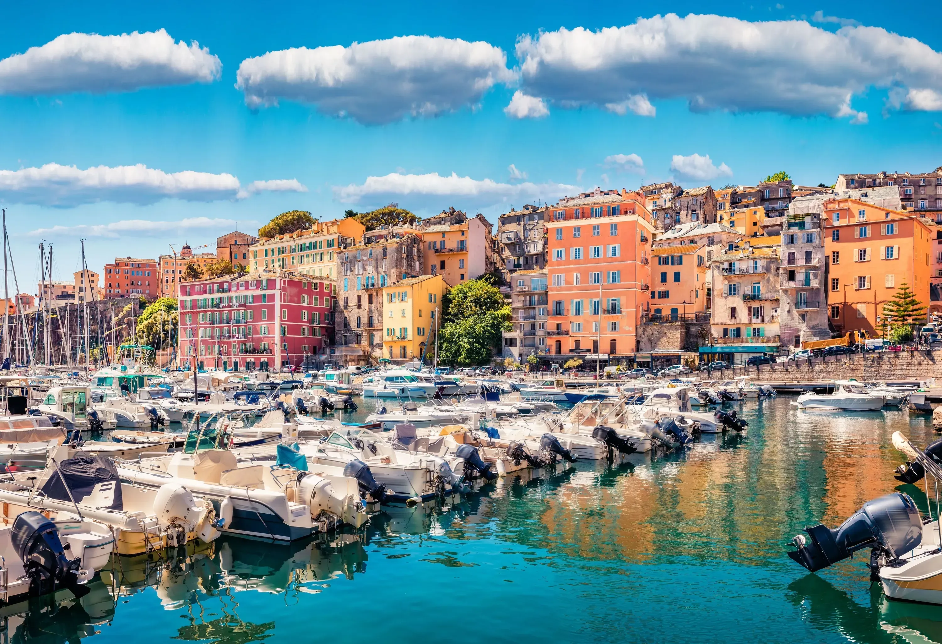 A vibrant seaside town with motorboats docked in the harbour and colourful buildings lining the coast.