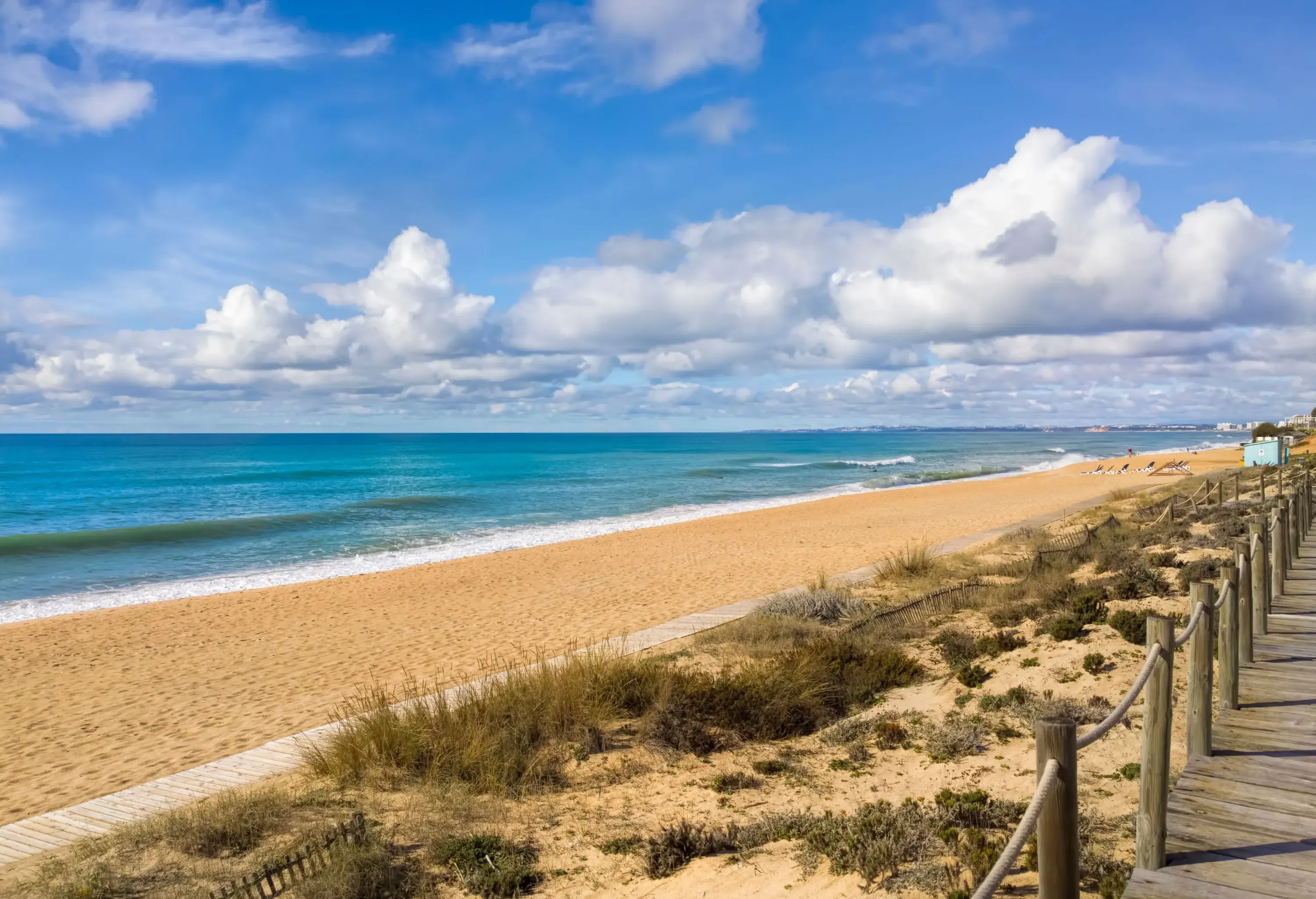 A beach with powdery sands stretching along the blue waters and a boardwalk across from it.